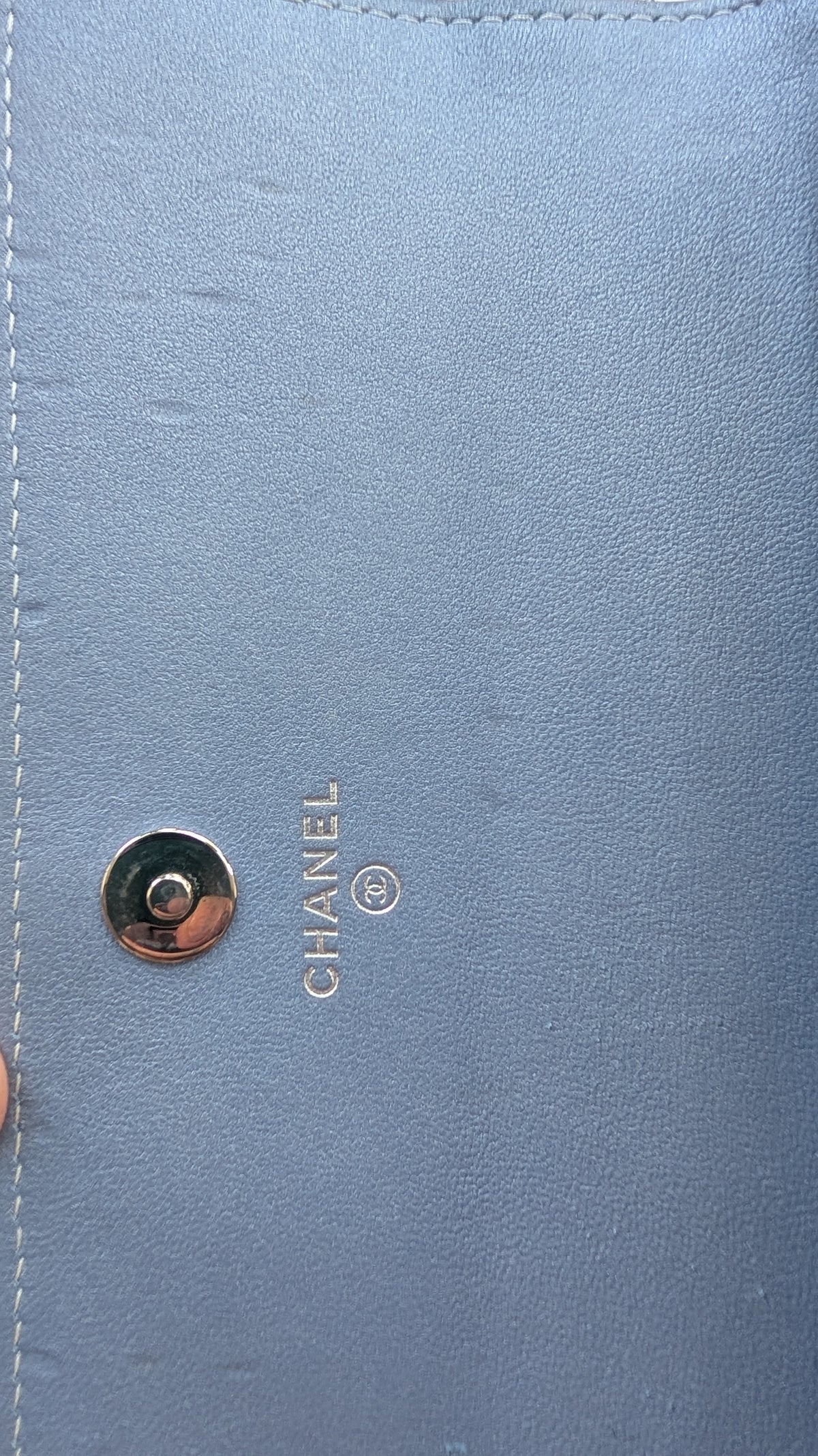 Close-up of a light blue leather Chanel bag with a gold-tone snap button and the embossed CHANEL logo. Pre-Owned Chanel Camellia Studded Wallet on Chain WOC – Blue Lambskin