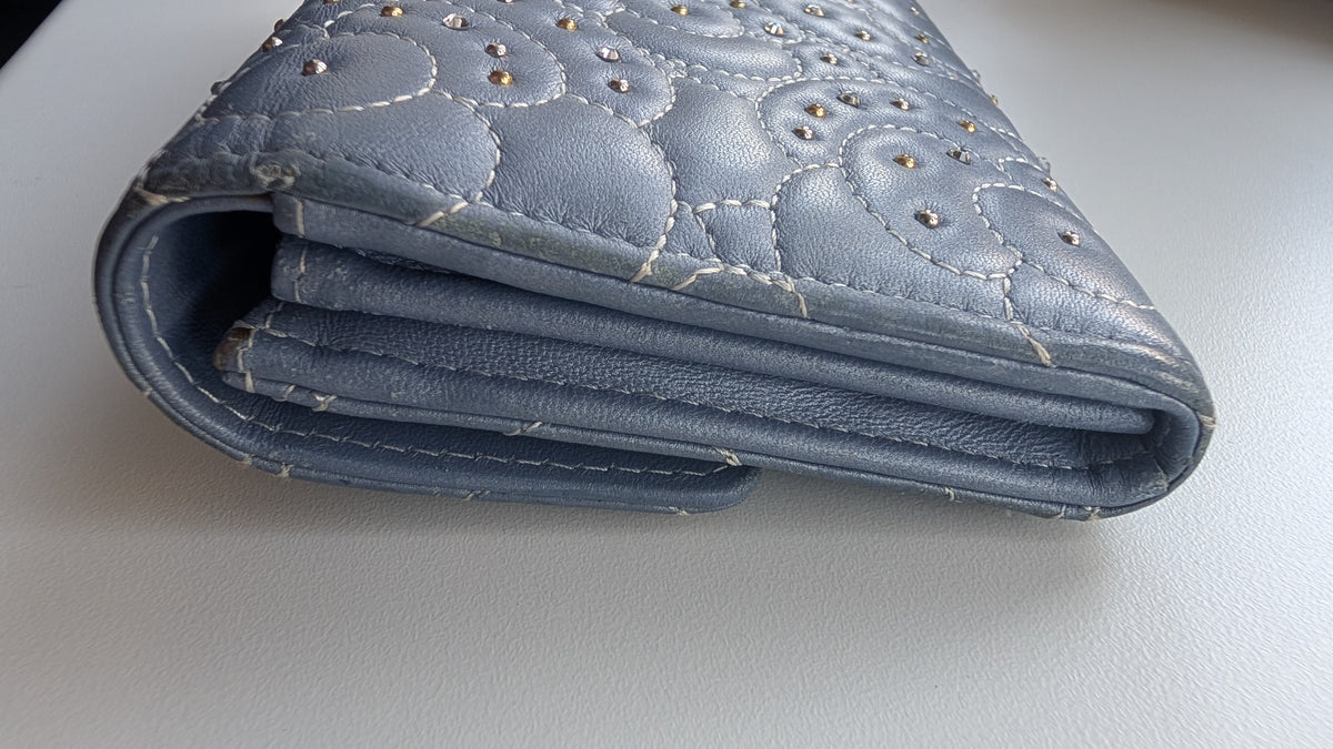 A close-up of a light blue quilted leather wallet with decorative studs and visible wear on the surface. Pre-Owned Chanel Camellia Studded Wallet on Chain WOC – Blue Lambskin