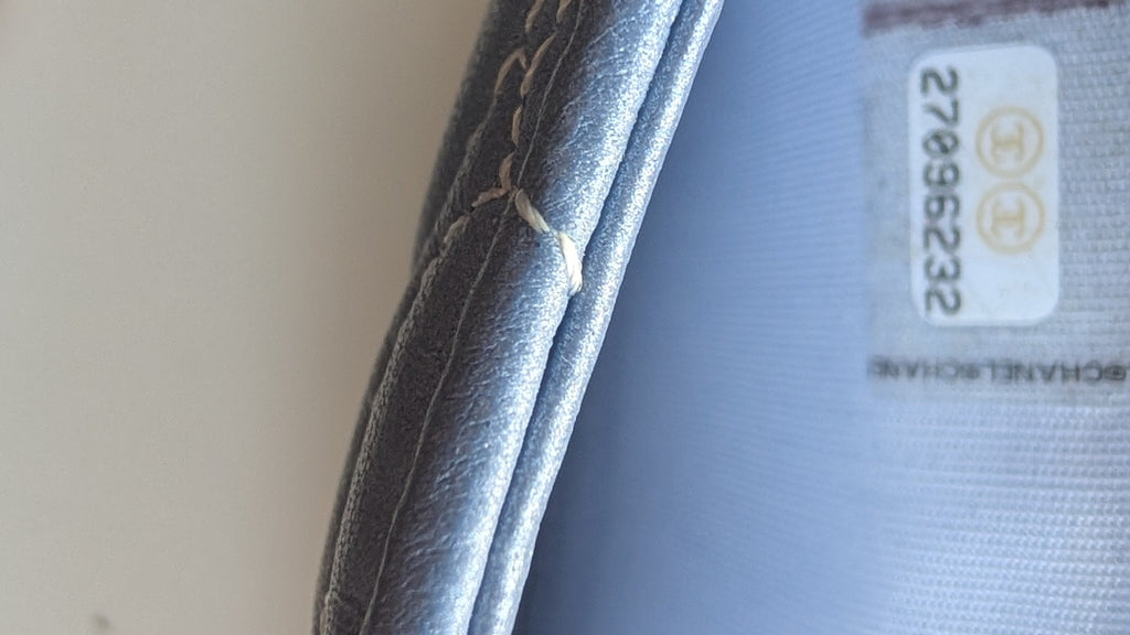 Close-up of a shoe interior showing a light blue fabric lining with a white size label and a finger holding the edge. Pre-Owned Chanel Camellia Studded Wallet on Chain WOC – Blue Lambskin