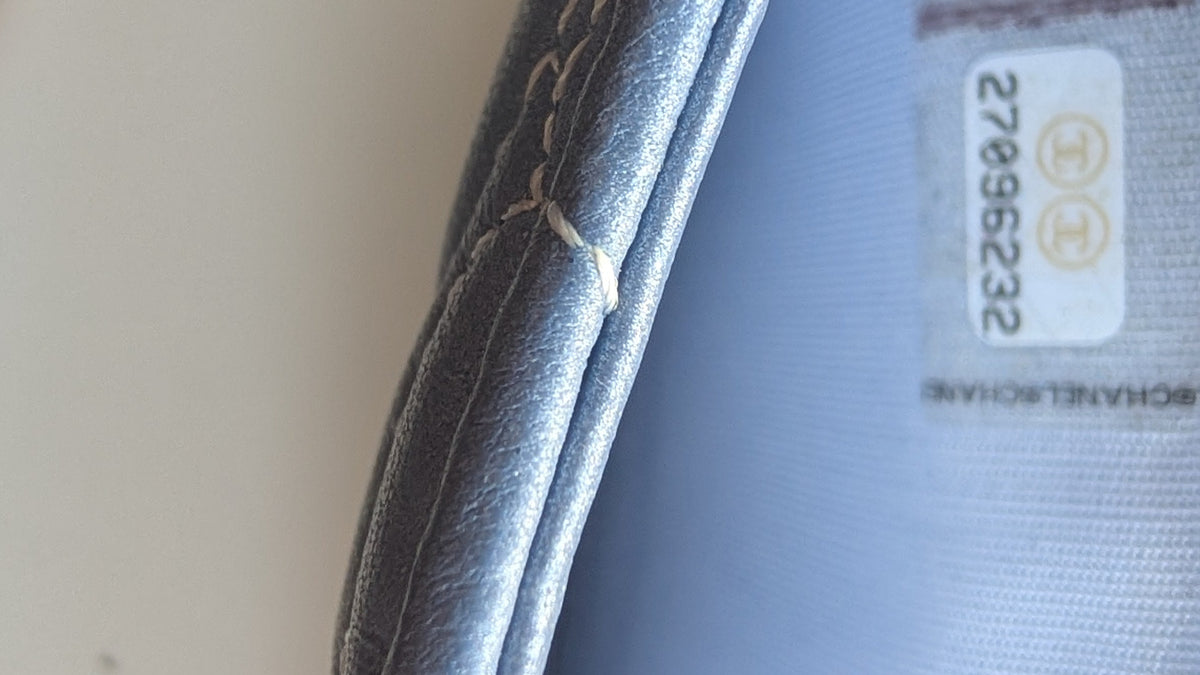 Close-up of a shoe interior showing a light blue fabric lining with a white size label and a finger holding the edge. Pre-Owned Chanel Camellia Studded Wallet on Chain WOC – Blue Lambskin