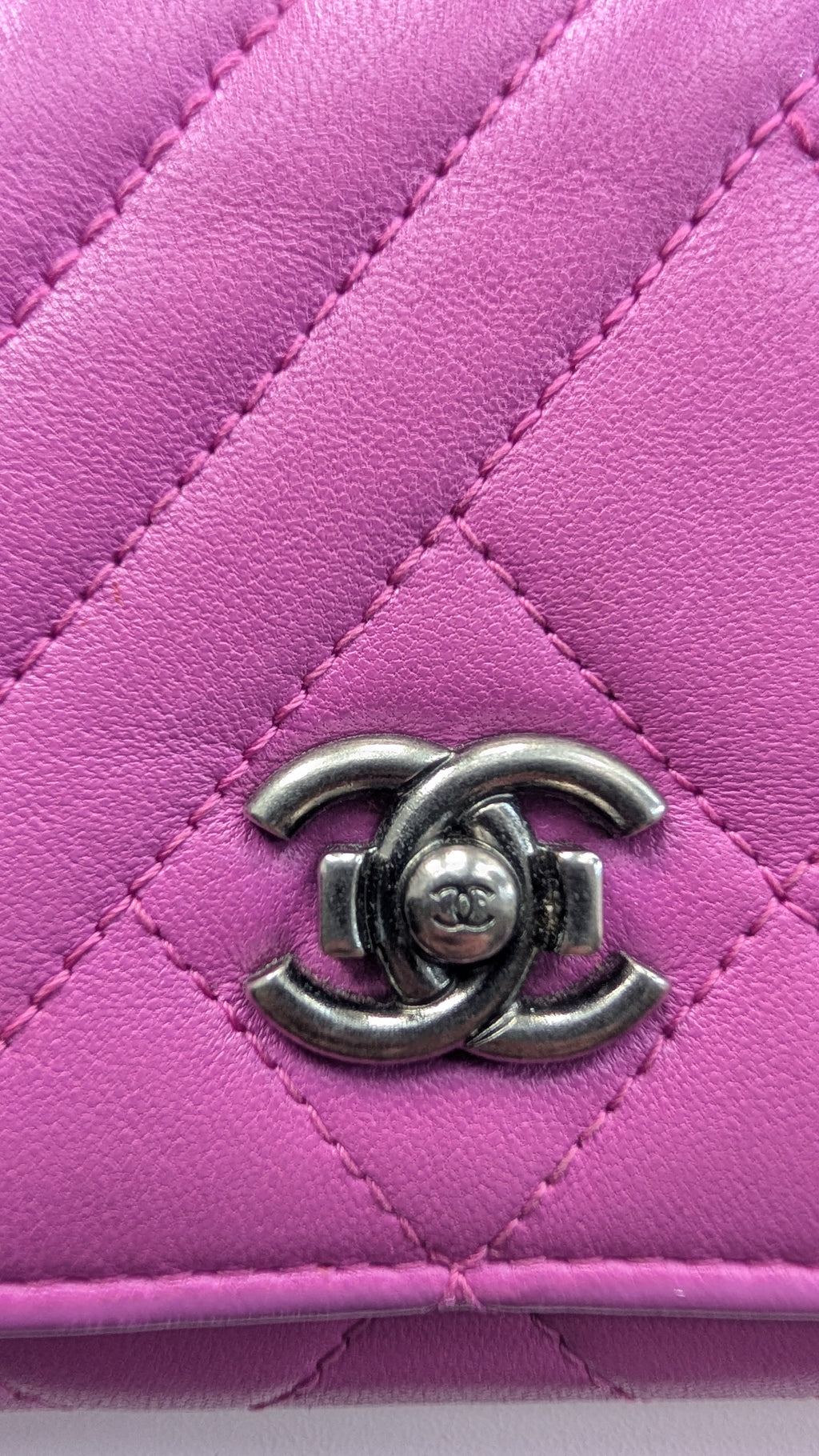 A close-up of a quilted pink leather wallet or clutch featuring a silver-tone interlocking CC logo clasp, characteristic of Chanel. Pre-Owned Chanel Quilted Wallet on Chain WOC – Pink/Purple Lambskin – Silver Hardware