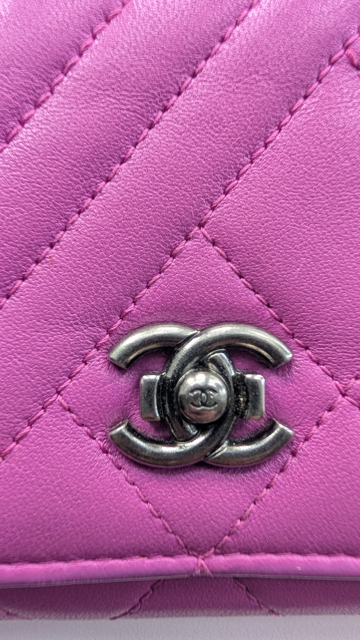 A close-up of a quilted pink leather wallet or clutch featuring a silver-tone interlocking CC logo clasp, characteristic of Chanel. Pre-Owned Chanel Quilted Wallet on Chain WOC – Pink/Purple Lambskin – Silver Hardware
