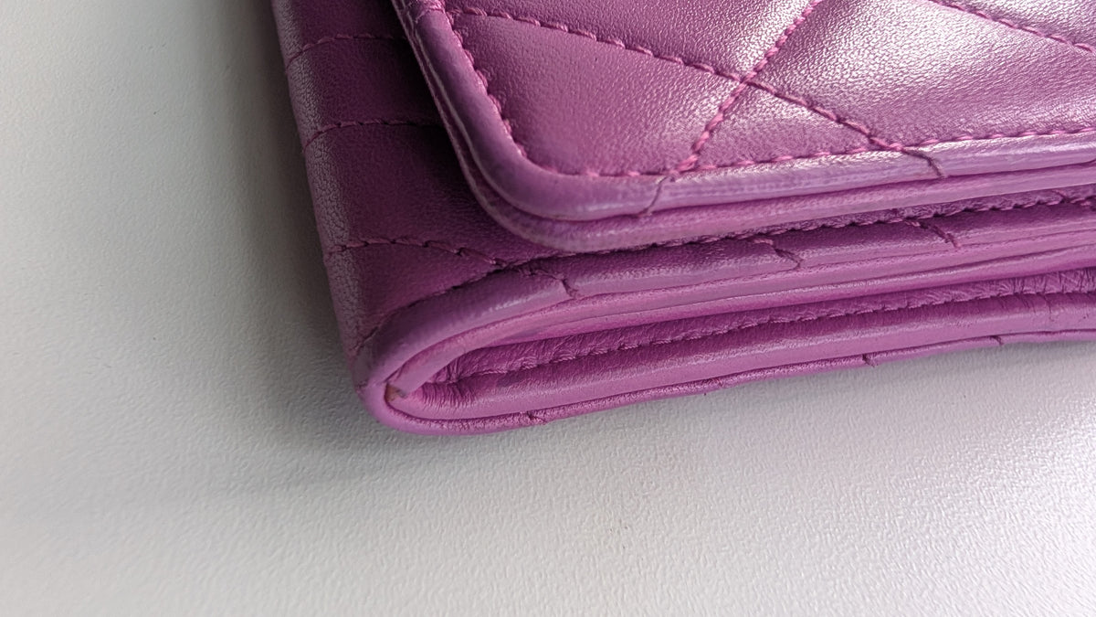 A close-up of a folded pink quilted leather wallet or clutch on a light gray Pre-Owned Chanel Quilted Wallet on Chain WOC – Pink/Purple Lambskin – Silver Hardwaresurface.