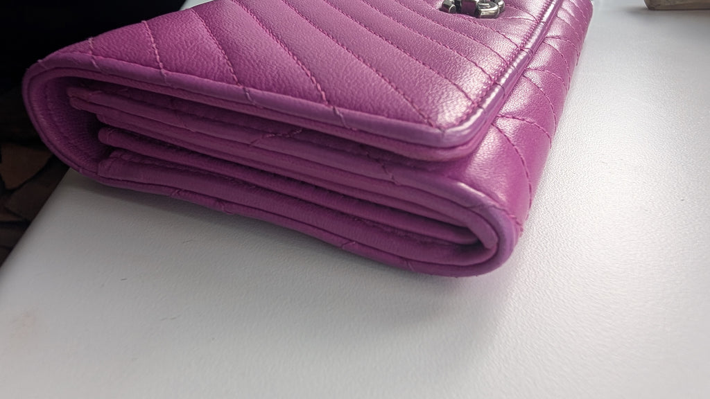 A folded magenta quilted leather wallet or clutch with silver-tone hardware, resting on a white surface. Pre-Owned Chanel Quilted Wallet on Chain WOC – Pink/Purple Lambskin – Silver Hardware