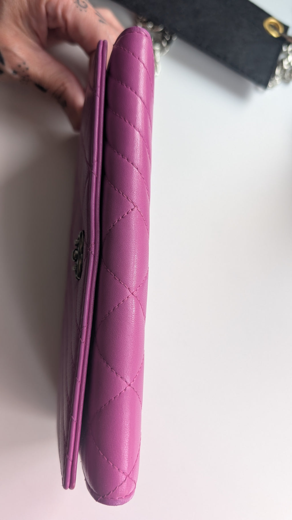 A close-up of a pink quilted leather wallet or clutch being held by a hand, showing the diamond-stitched texture and a small metal logo clasp on a white surface.Pre-Owned Chanel Quilted Wallet on Chain WOC – Pink/Purple Lambskin – Silver Hardware