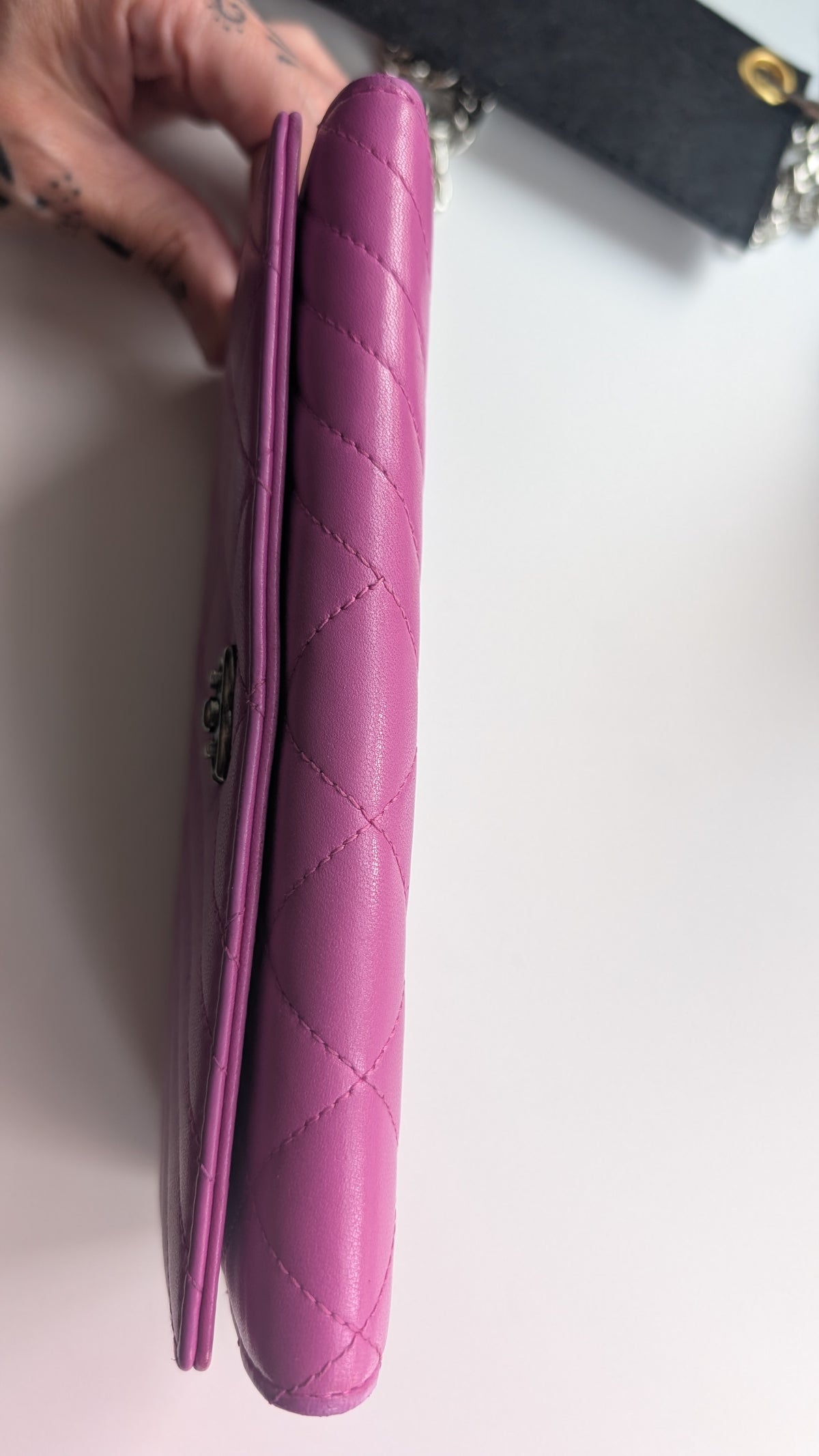 A close-up of a pink quilted leather wallet or clutch being held by a hand, showing the diamond-stitched texture and a small metal logo clasp on a white surface.Pre-Owned Chanel Quilted Wallet on Chain WOC – Pink/Purple Lambskin – Silver Hardware