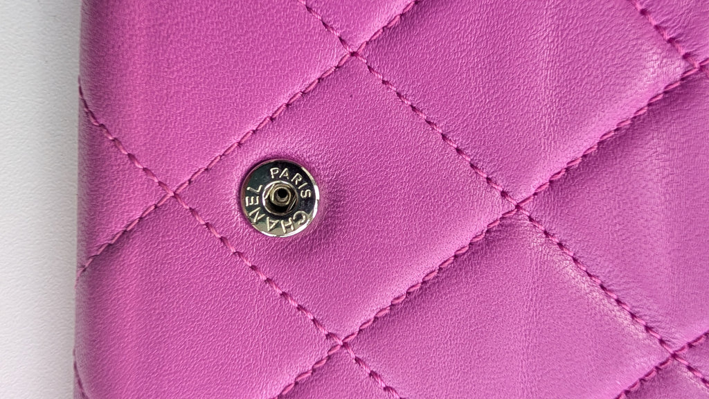 A close-up of a pink quilted leather wallet or clutch featuring a silver-tone Chanel Paris snap button closure. Pre-Owned Chanel Quilted Wallet on Chain WOC – Pink/Purple Lambskin – Silver Hardware