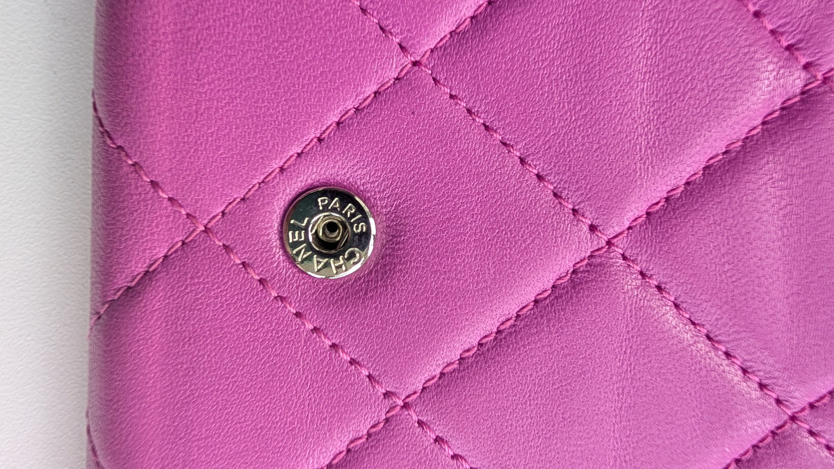 A close-up of a pink quilted leather wallet or clutch featuring a silver-tone Chanel Paris snap button closure. Pre-Owned Chanel Quilted Wallet on Chain WOC – Pink/Purple Lambskin – Silver Hardware