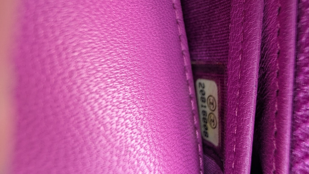 Close-up of a bright pink textured leather surface with visible stitching and a small interior tag. Pre-Owned Chanel Quilted Wallet on Chain WOC – Pink/Purple Lambskin – Silver Hardware