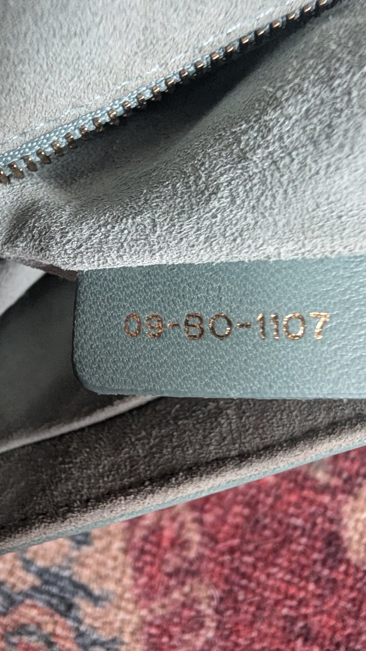 Close-up of a light blue-gray suede or microfiber pouch with a zipper and a sewn-on label stamped with the gold-colored serial number '09-50-1107'. Pre-Owned Christian Dior Small DiorAddict Cannage Studded Flap Bag – Light Blue Lambskin