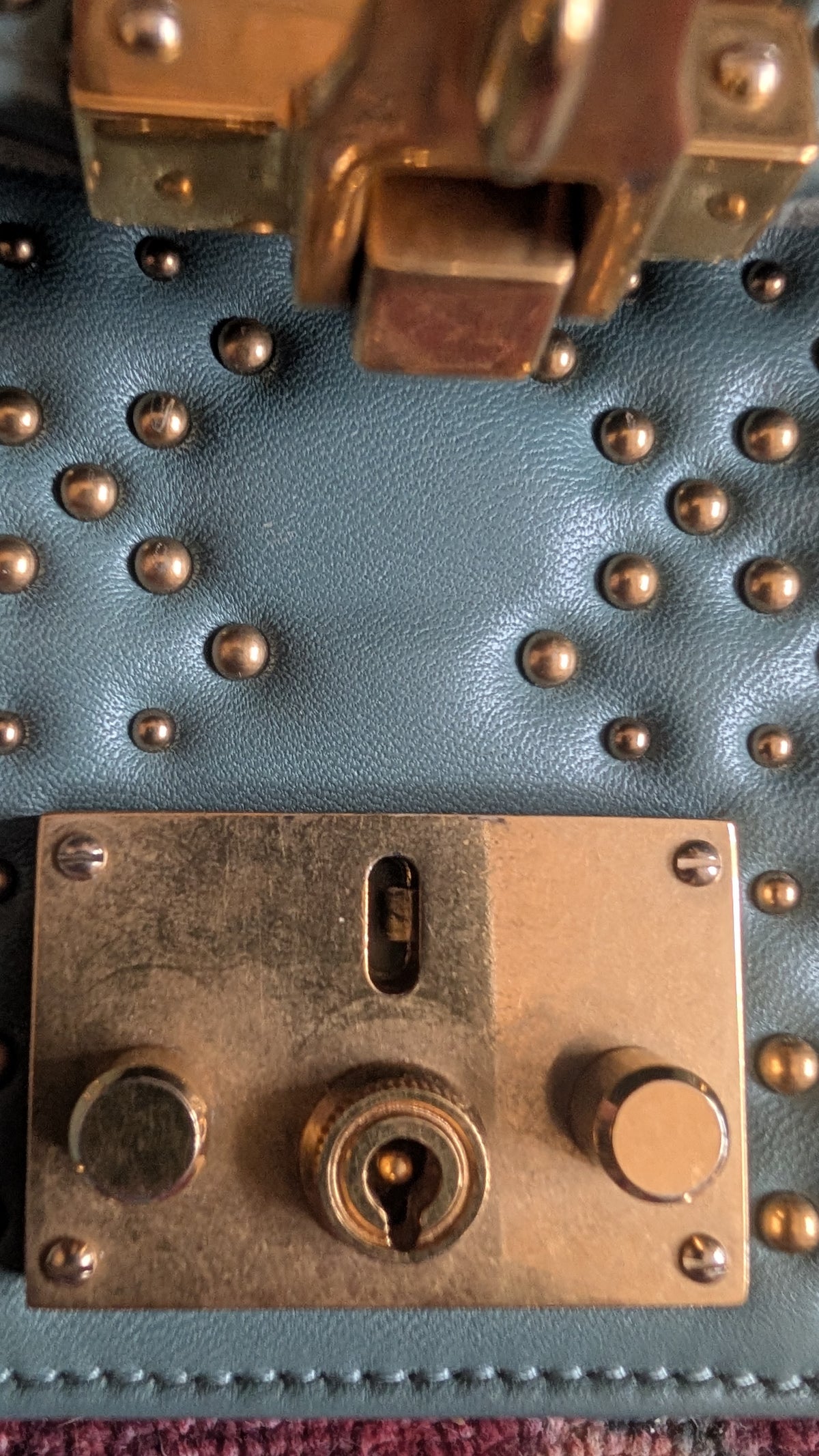 Close-up of a textured blue leather handbag with bronze studs and a large bronze metal clasp lock. Pre-Owned Christian Dior Small DiorAddict Cannage Studded Flap Bag – Light Blue Lambskin