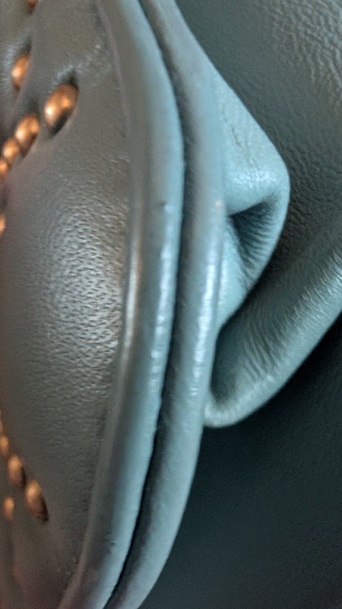 Close-up of a textured leather handbag in a muted blue-green color with gold-tone studs and chain details. Pre-Owned Christian Dior Small DiorAddict Cannage Studded Flap Bag – Light Blue Lambskin