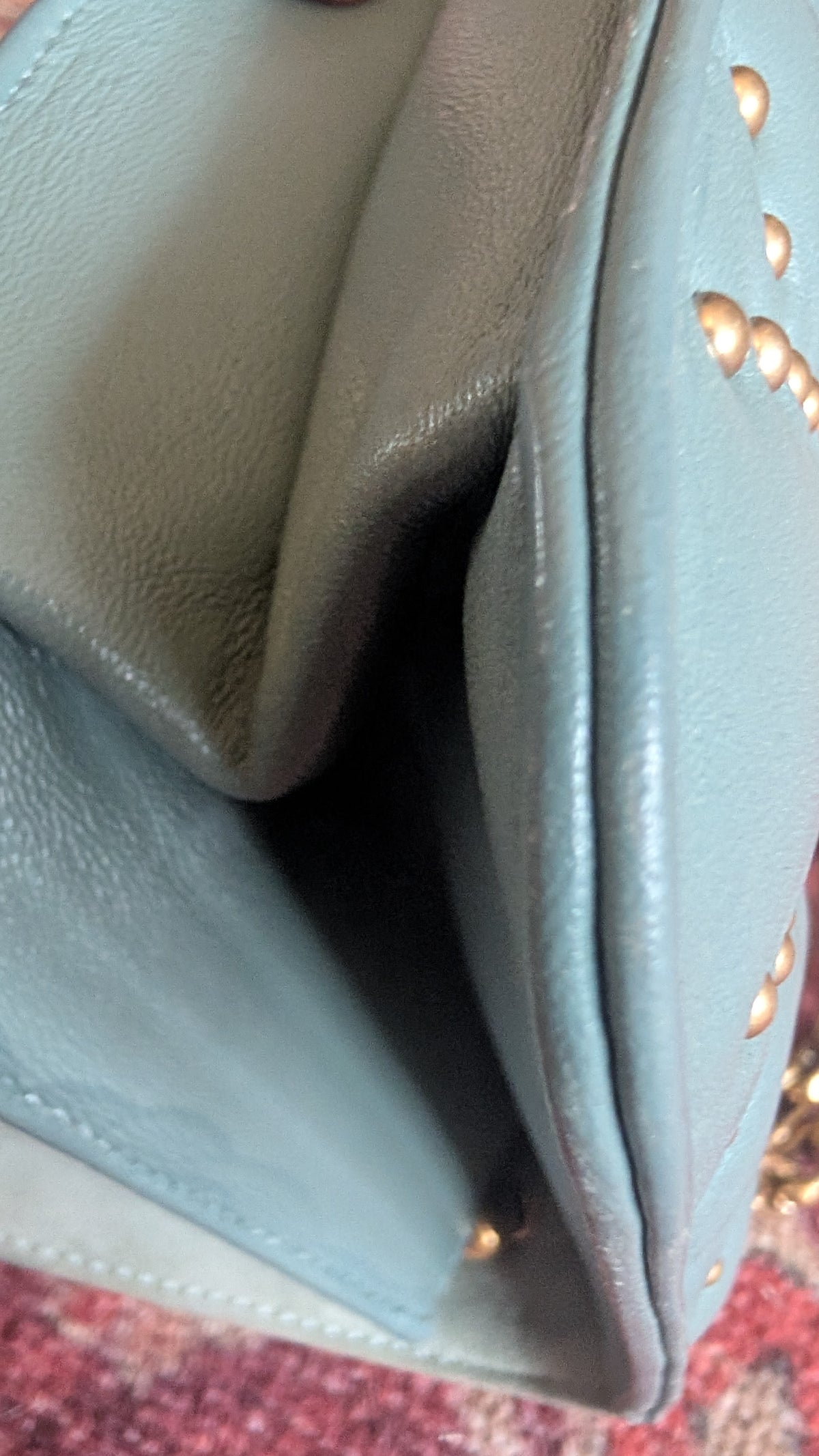 Close-up of a light blue leather clutch or wallet with gold-tone studs, showing the pebbled texture and interior fold. Pre-Owned Christian Dior Small DiorAddict Cannage Studded Flap Bag – Light Blue Lambskin