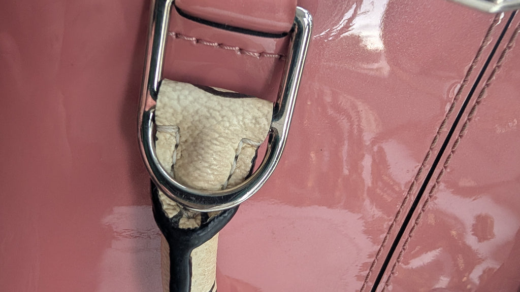 Close-up of a dusty pink leather bag featuring a polished silver-tone metal D-ring with a beige textured fabric insert and a black-and-beige strap. Pre-Owned LOUIS VUITTON ALMA BB – ROSE BLUSH MONOGRAM VERNIS MIROIR