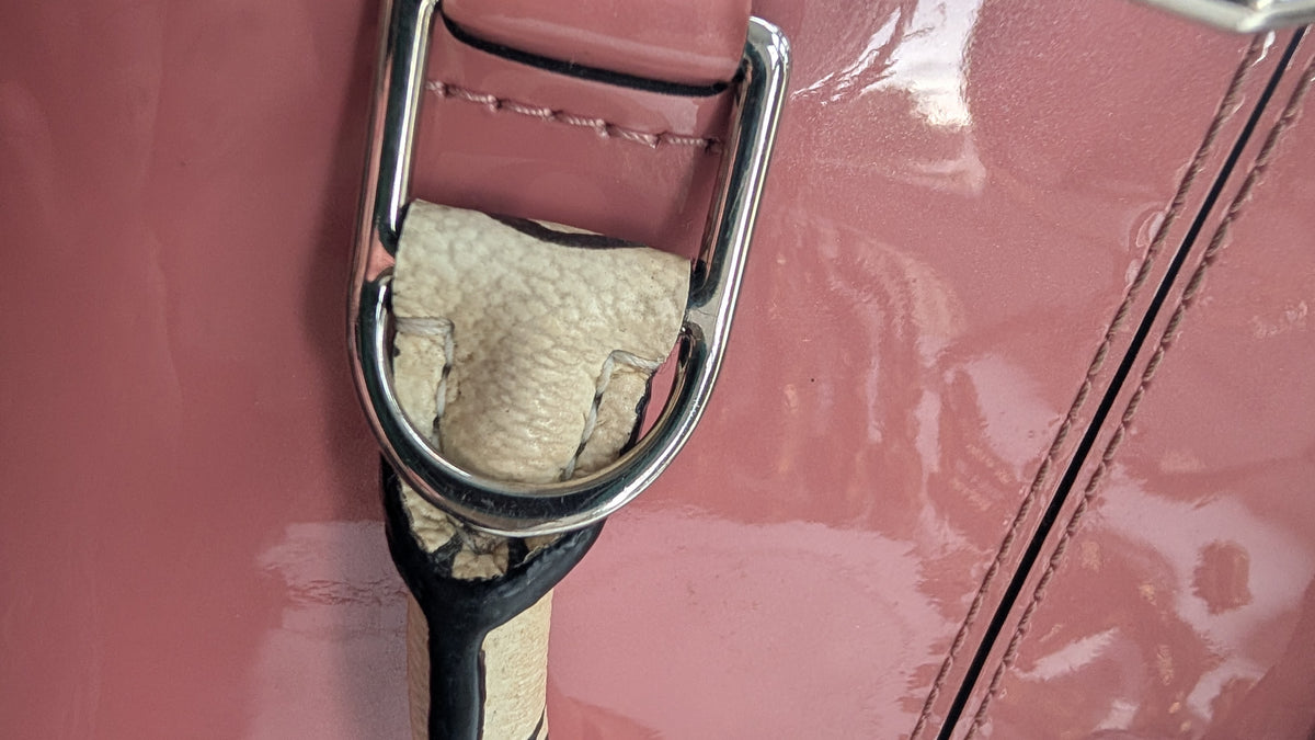 Close-up of a dusty pink leather bag featuring a polished silver-tone metal D-ring with a beige textured fabric insert and a black-and-beige strap. Pre-Owned LOUIS VUITTON ALMA BB – ROSE BLUSH MONOGRAM VERNIS MIROIR