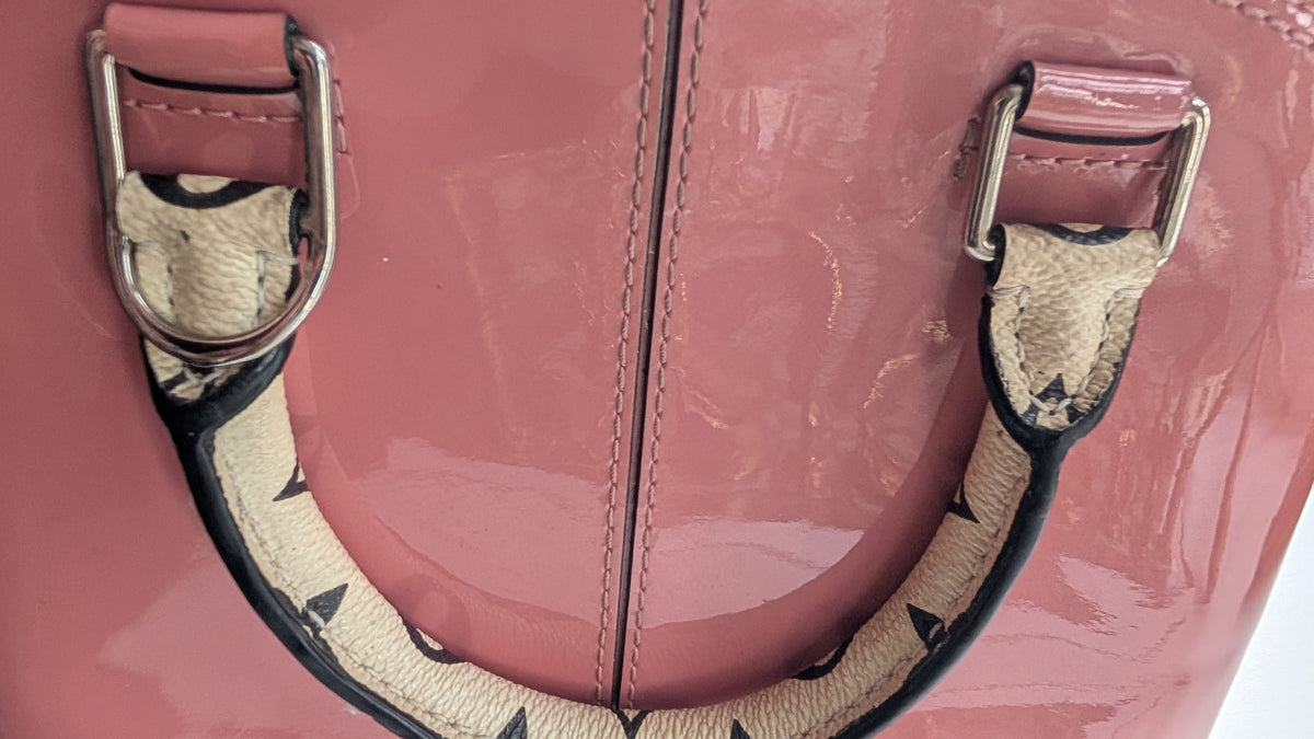 Close-up of a pink patent leather handbag with silver-tone hardware and a beige-and-black patterned strap detail. Pre-Owned LOUIS VUITTON ALMA BB – ROSE BLUSH MONOGRAM VERNIS MIROIR