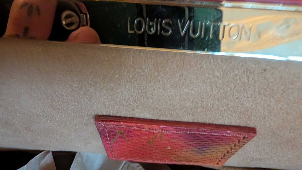 Close-up of a Louis Vuitton handbag or pouch showing a beige textured leather flap, a metallic silver brand plaque with 'LOGIS VUITTON' engraved, and a pink gradient leather accent tab. Pre-Owned Louis Vuitton x Richard Prince Limited Edition Monogram Aquarelle Watercolor Frame Speedy 30 – 2008
