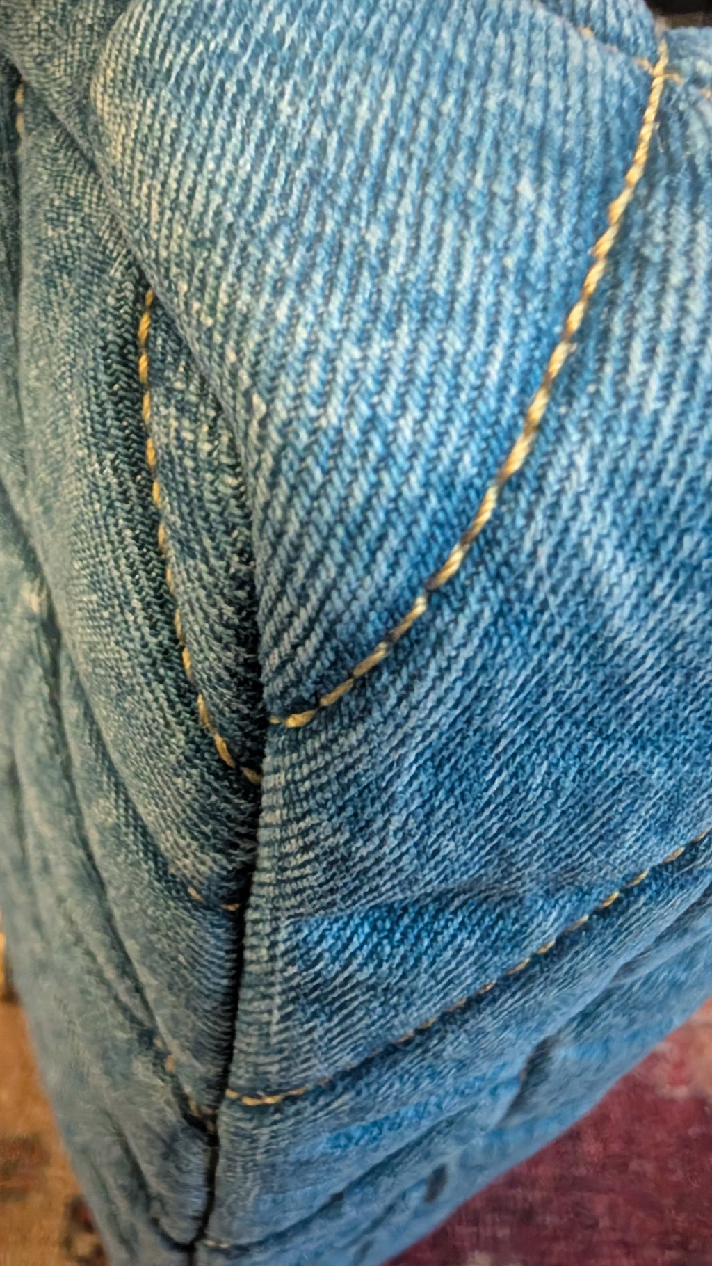 Close-up of a blue denim fabric surface with visible diagonal twill texture and contrast gold stitching along the fold. Pre-Owned Coach Quilted Tabby Shoulder Bag 26 – Blue Denim