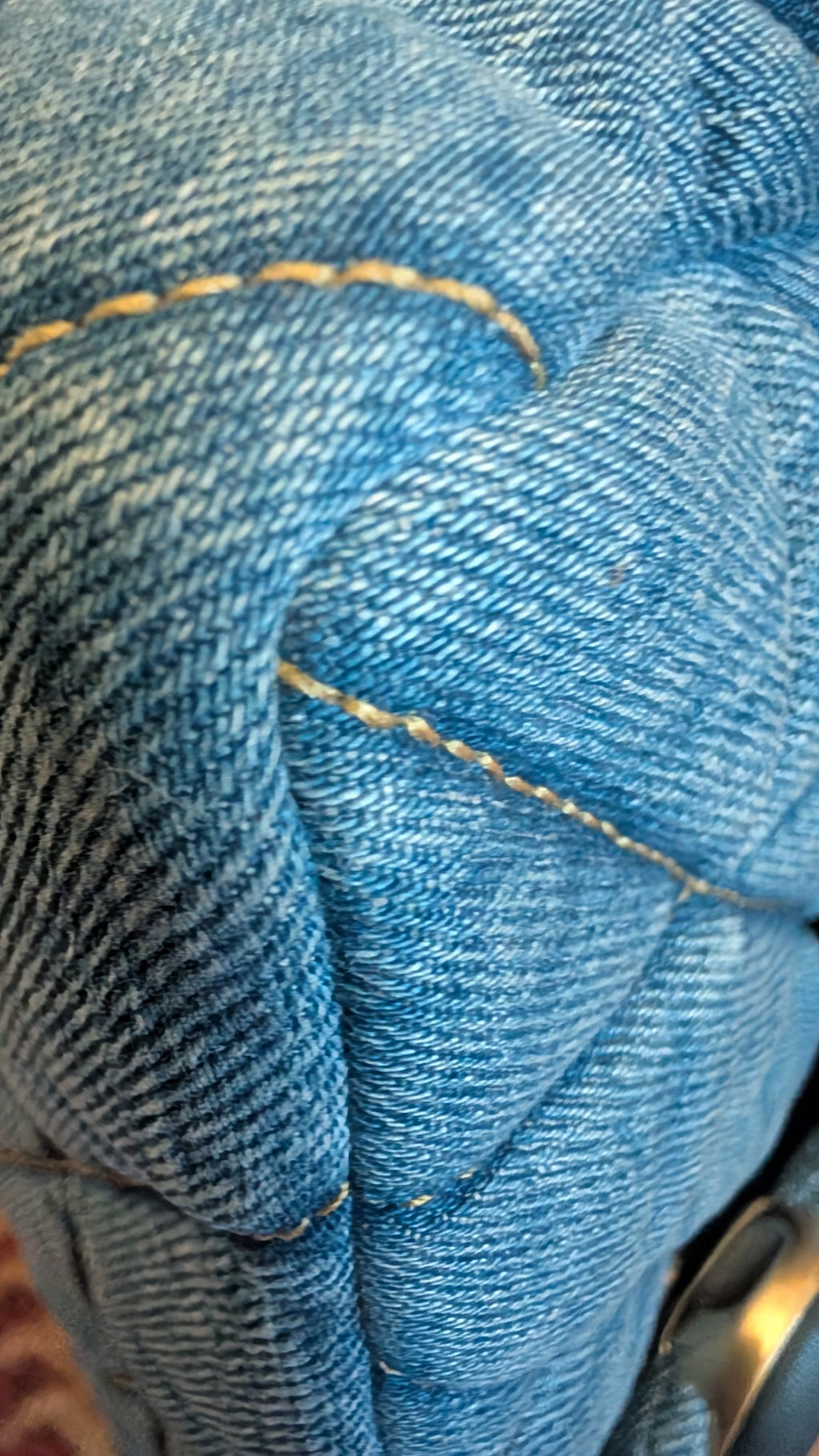 Close-up of blue denim fabric with visible diagonal twill texture and contrast yellow stitching. Pre-Owned Coach Quilted Tabby Shoulder Bag 26 – Blue Denim