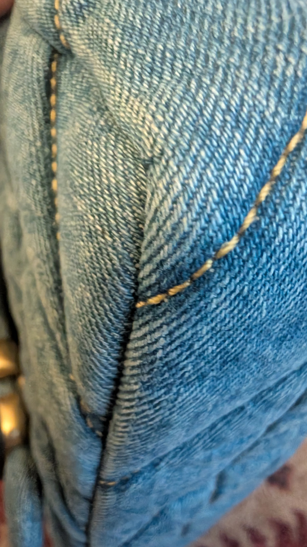 Close-up of blue denim fabric with visible diagonal twill texture and contrast yellow stitching. Pre-Owned Coach Quilted Tabby Shoulder Bag 26 – Blue Denim