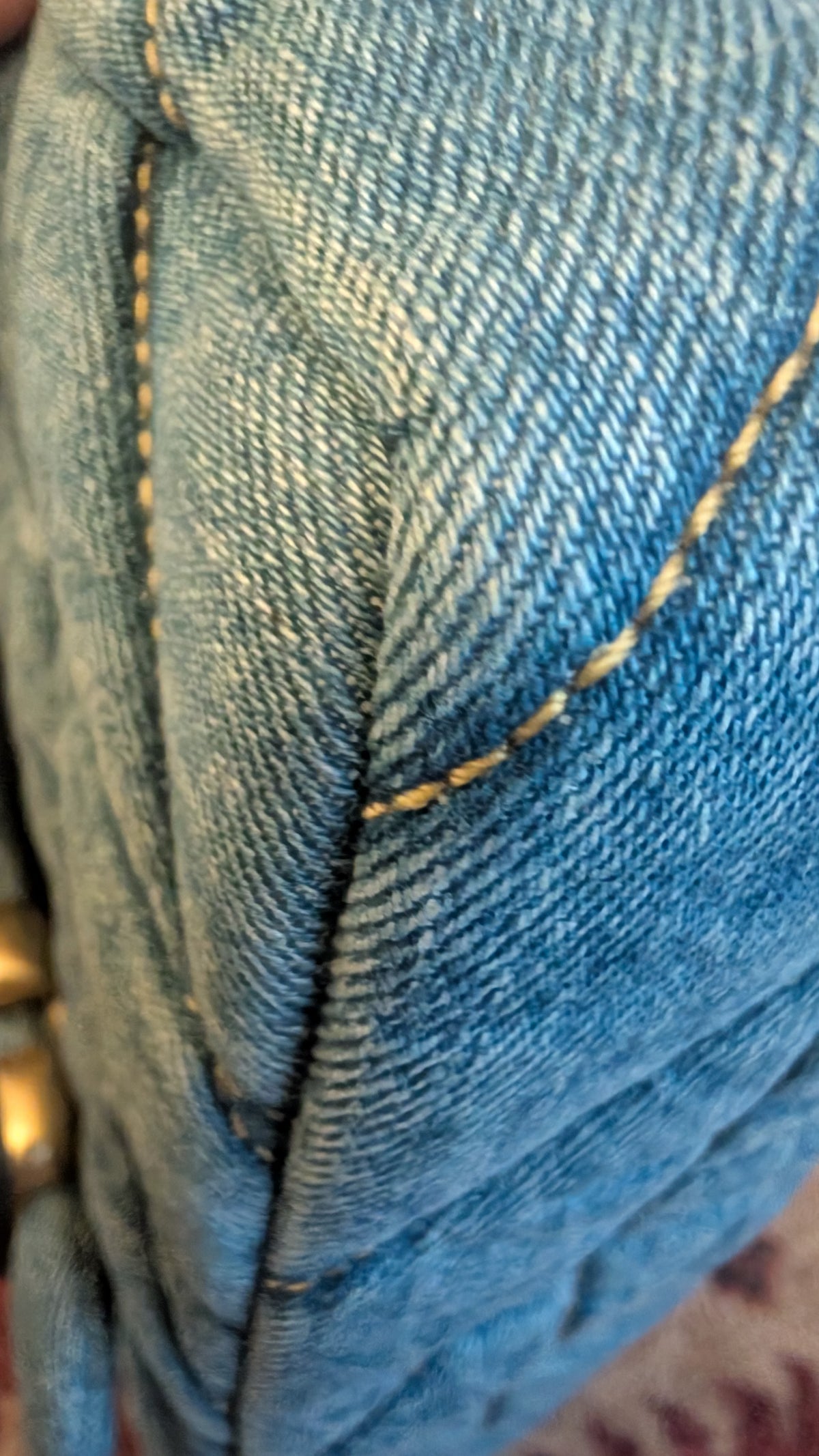 Close-up of blue denim fabric with visible diagonal twill texture and contrast yellow stitching. Pre-Owned Coach Quilted Tabby Shoulder Bag 26 – Blue Denim