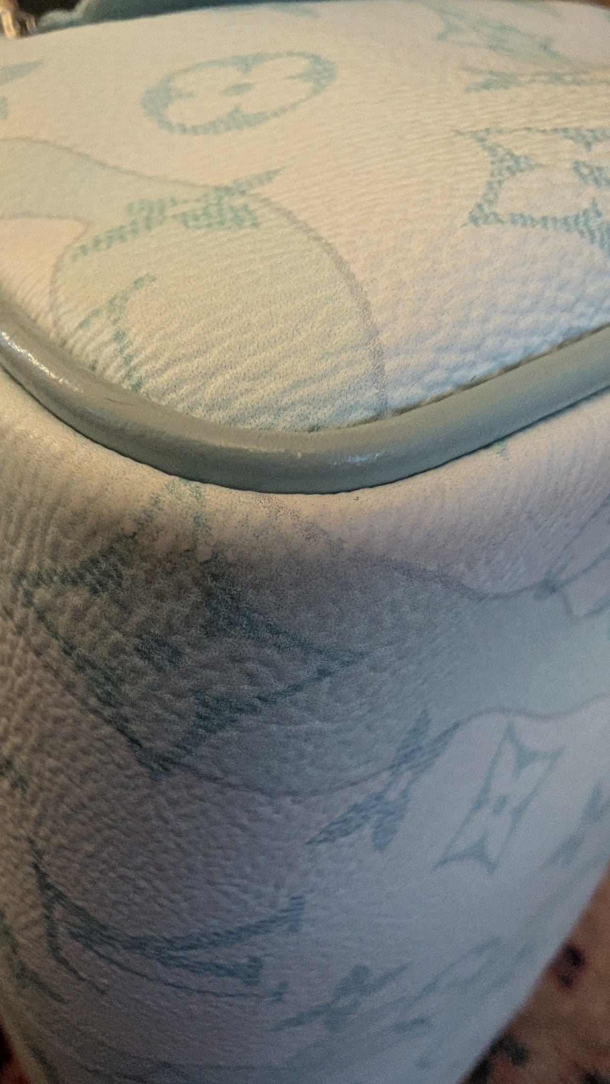 Close-up of a light-colored textured fabric surface with a pale blue monogram-style pattern and a matching blue trim edge. Pre-Owned Louis Vuitton x Richard Prince Limited Edition Monogram Bag – Spring/Summer 2008 – Pale Blue