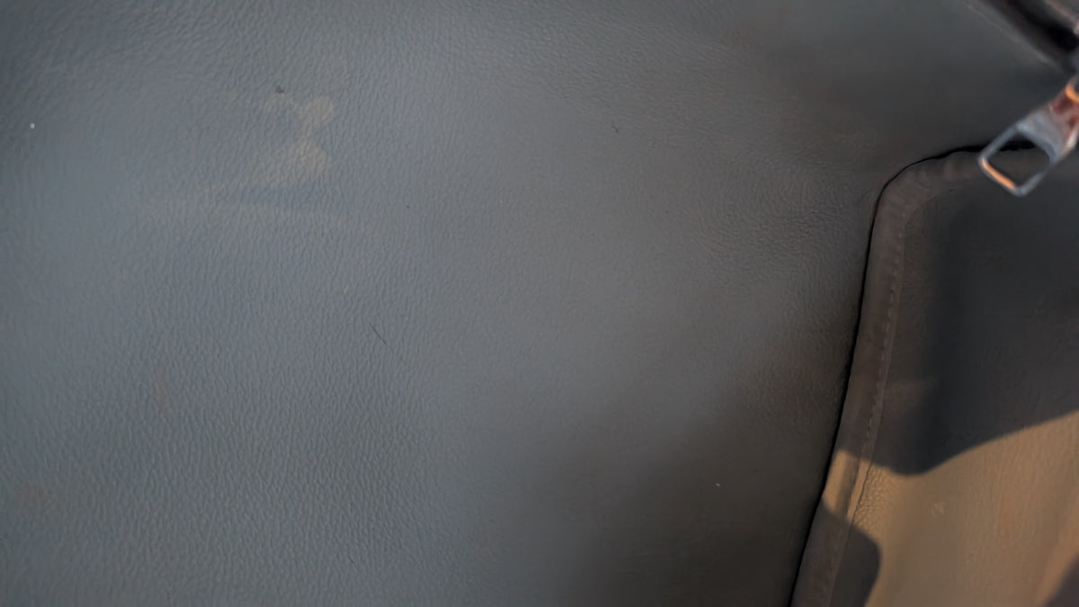 Close-up of a dark gray textured leather or faux-leather surface with a black stitched edge and a small metallic pull tab visible on the right.  Pre-Owned Louis Vuitton x Richard Prince Limited Edition Monogram Bag – Spring/Summer 2008 – Pale Blue