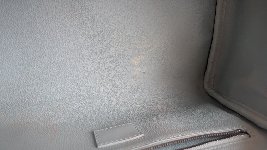 Close-up of the interior lining of a light gray textured leather bag, showing a small white stitched label and a zipper. Pre-Owned Louis Vuitton x Richard Prince Limited Edition Monogram Bag – Spring/Summer 2008 – Pale Blue
