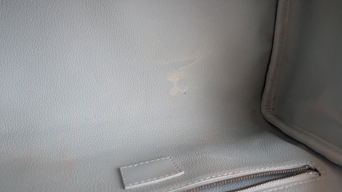 Close-up of the interior lining of a light gray textured leather bag, showing a small white stitched label and a zipper. Pre-Owned Louis Vuitton x Richard Prince Limited Edition Monogram Bag – Spring/Summer 2008 – Pale Blue