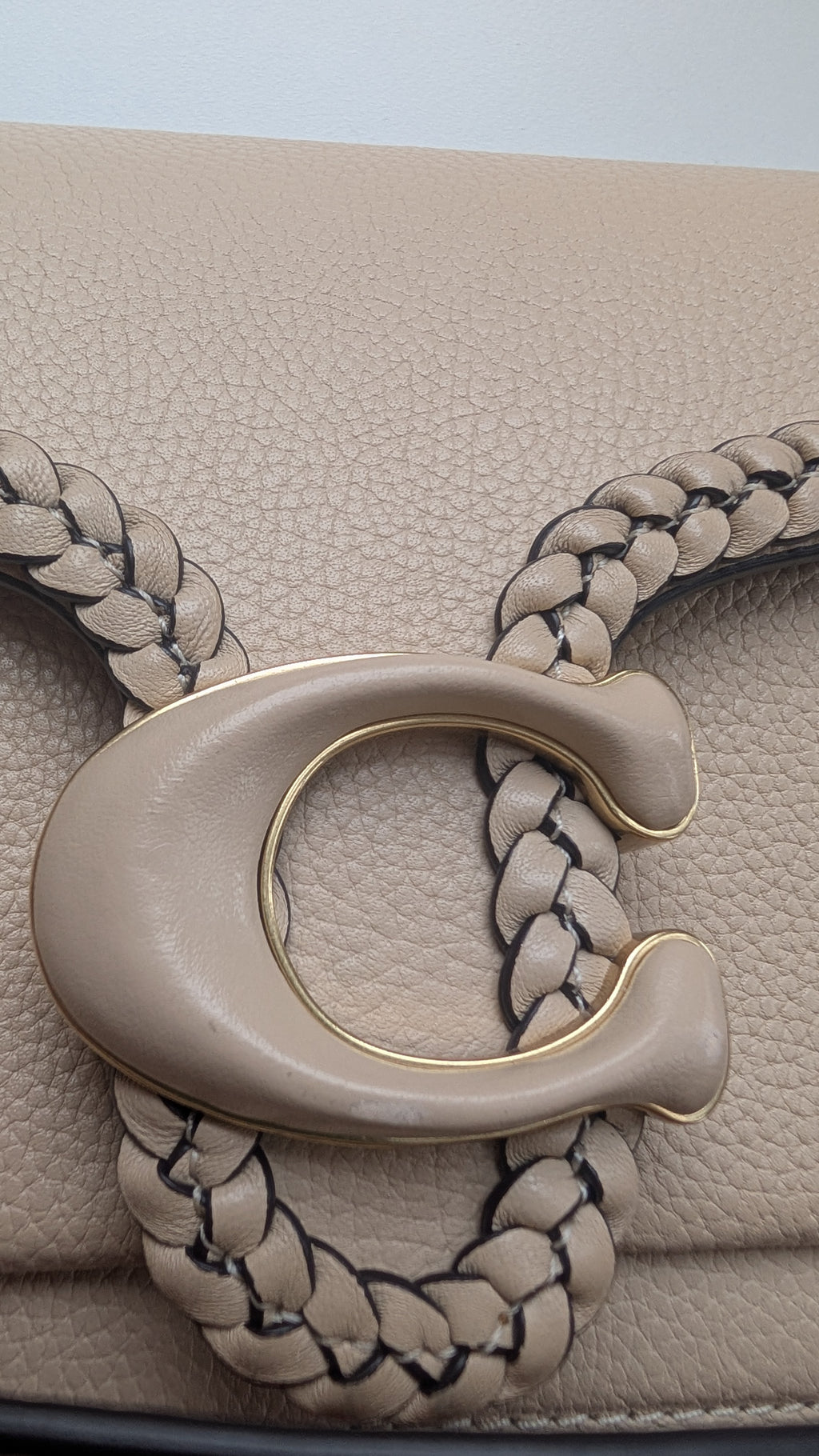 Close-up of a beige leather handbag featuring a large C-shaped metal clasp with a braided strap design. Pre-Owned Coach Tabby Braided Leather Shoulder Bag – Beige