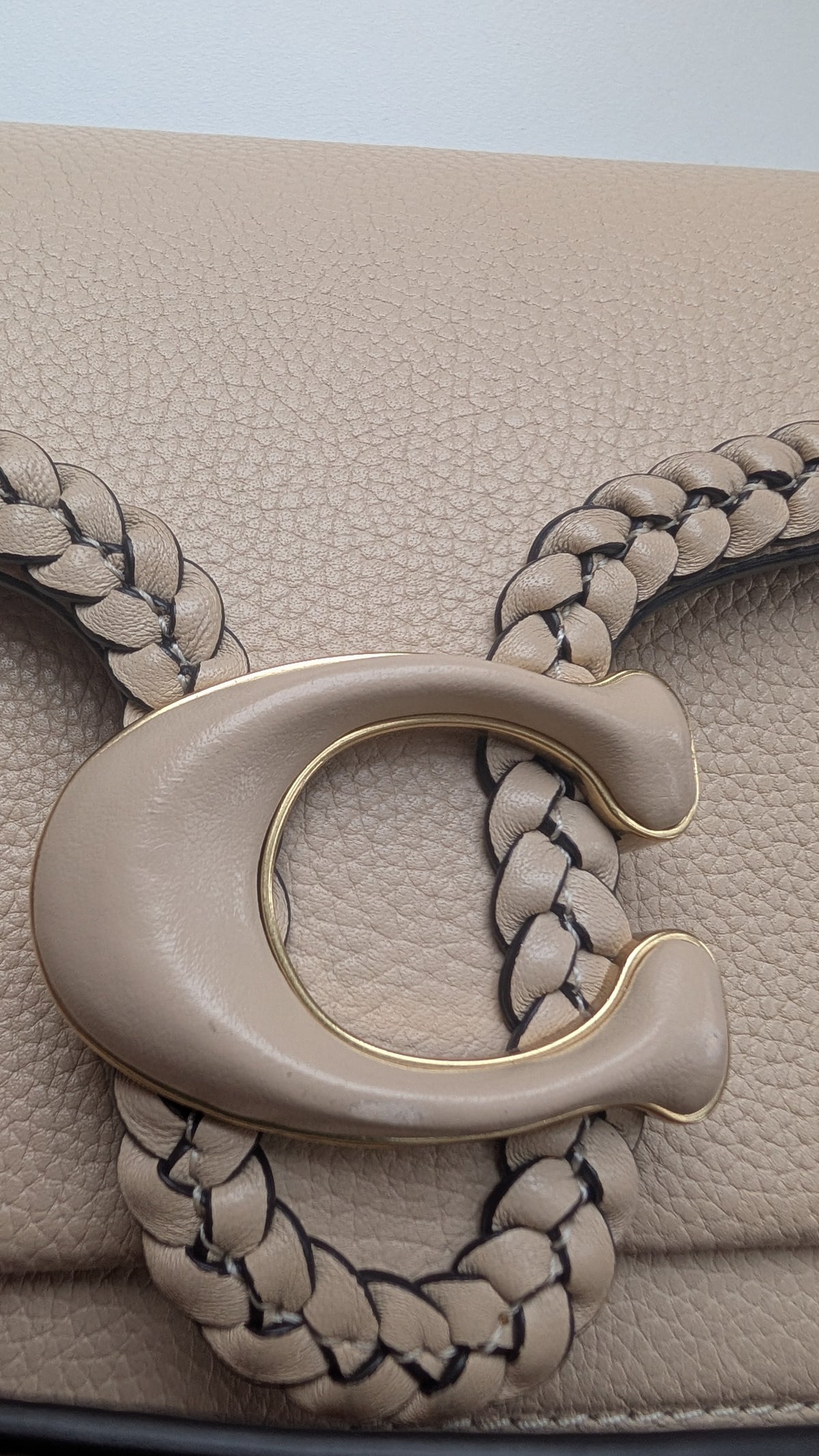 Close-up of a beige leather handbag featuring a large C-shaped metal clasp with a braided strap design. Pre-Owned Coach Tabby Braided Leather Shoulder Bag – Beige