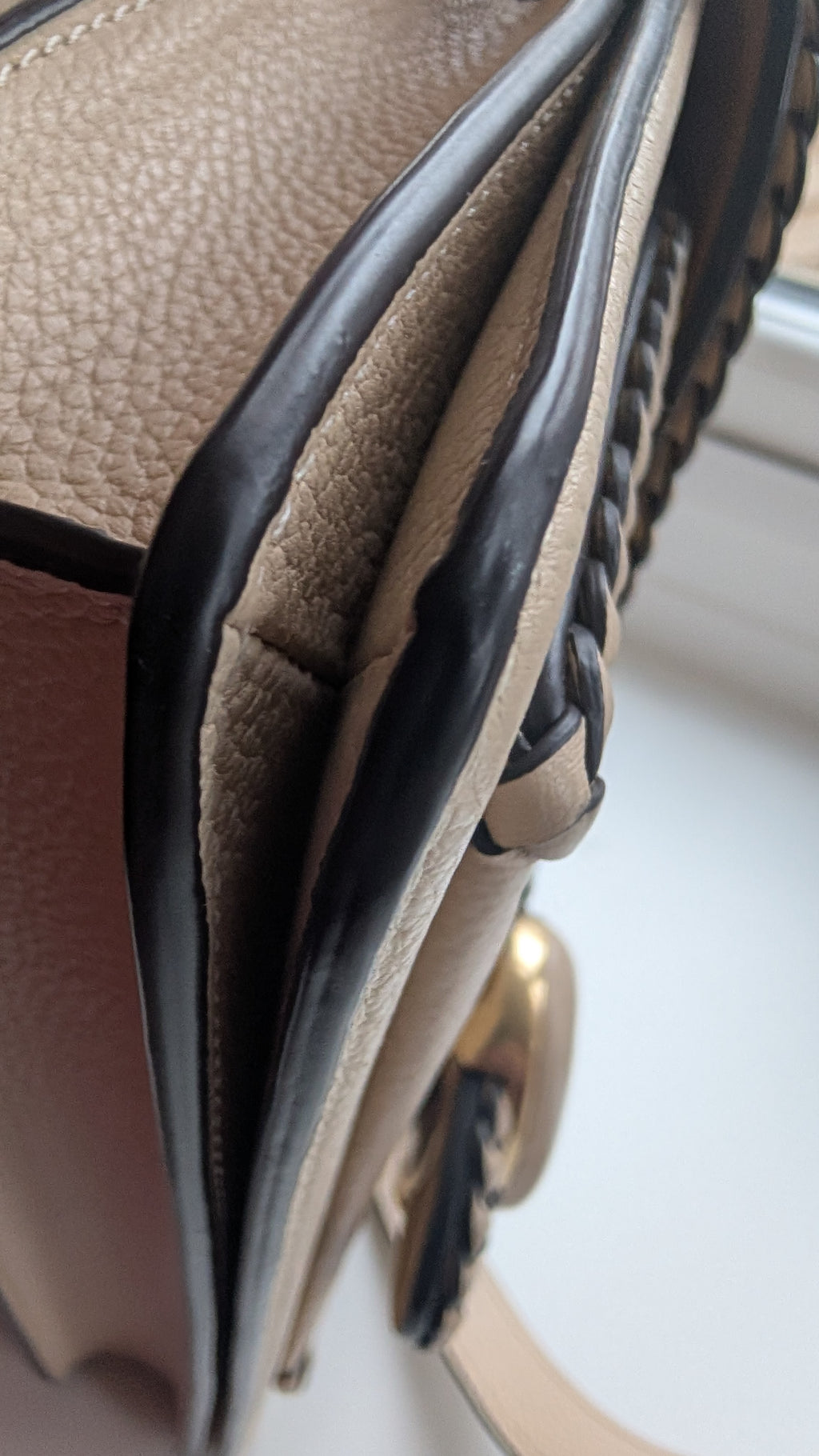 Close-up detail of a beige pebbled leather handbag showing the interior flap, black leather trim, braided strap detail, and a gold-tone hardware accent. Pre-Owned Coach Tabby Braided Leather Shoulder Bag – Beige