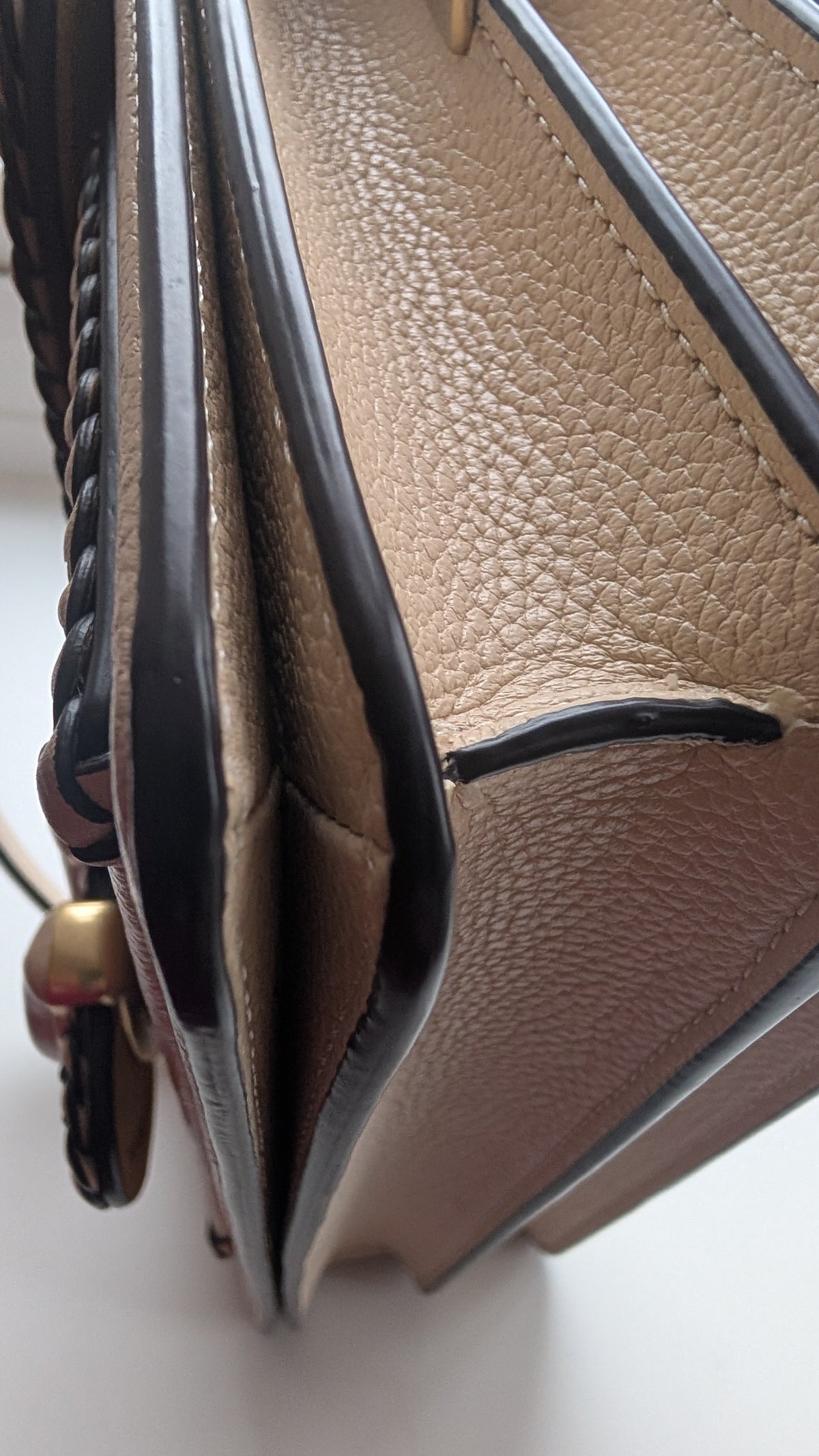 Close-up of a beige pebbled leather handbag showing the interior lining, black trim, and a braided strap detail. Pre-Owned Coach Tabby Braided Leather Shoulder Bag – Beige