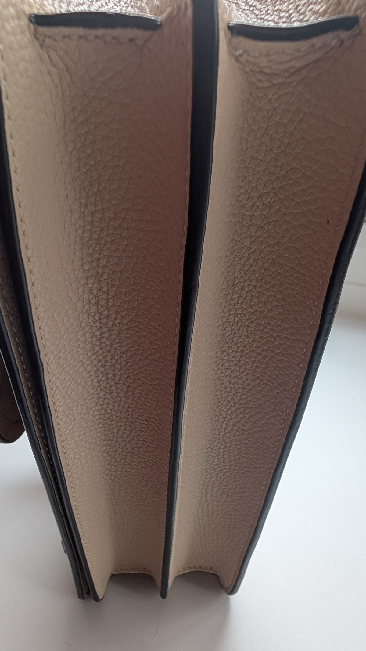 Close-up of the side profile of a beige pebbled leather BAG, showing the texture and black edge trim. Pre-Owned Coach Tabby Braided Leather Shoulder Bag – Beige