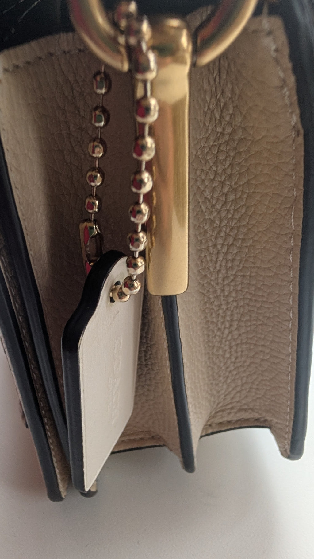 Close-up detail of a beige pebbled leather handbag with black trim, a gold-tone metal key ring, and a hanging gold-tone keychain tag. Pre-Owned Coach Tabby Braided Leather Shoulder Bag – Beige