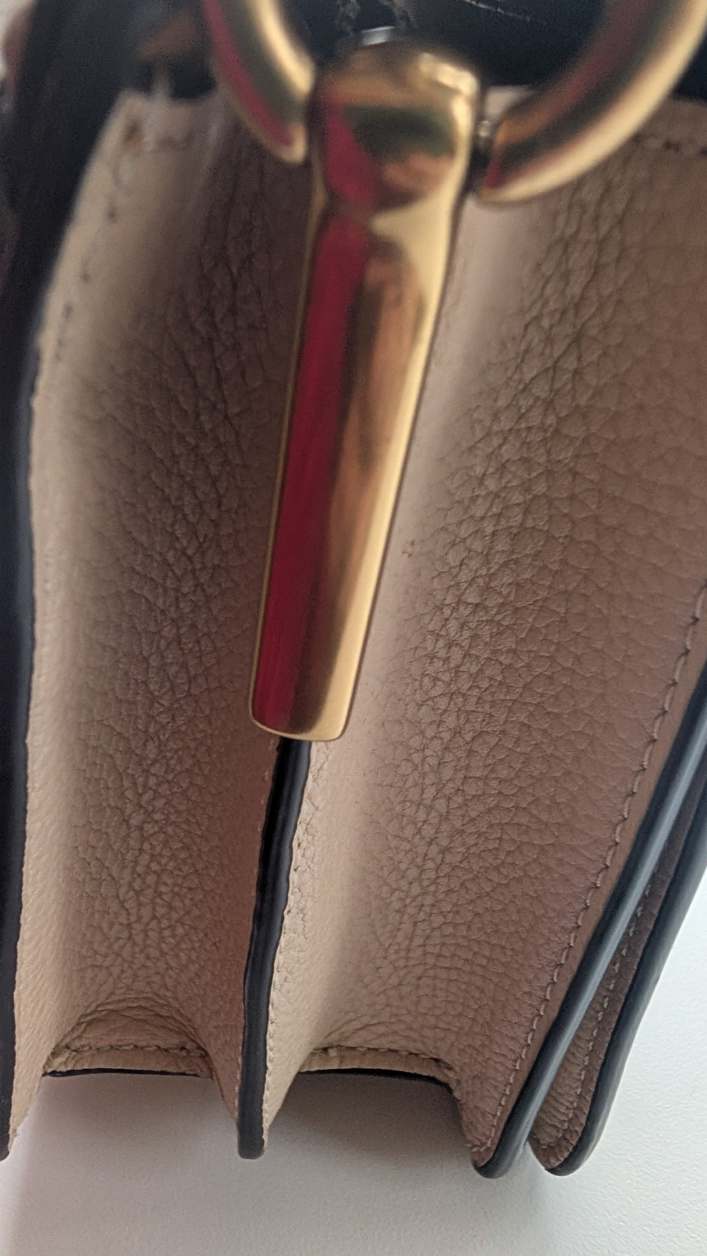 Close-up detail of a handbag showing textured beige leather panels, dark edging, and a polished gold-tone metal hardware piece. Pre-Owned Coach Tabby Braided Leather Shoulder Bag – Beige