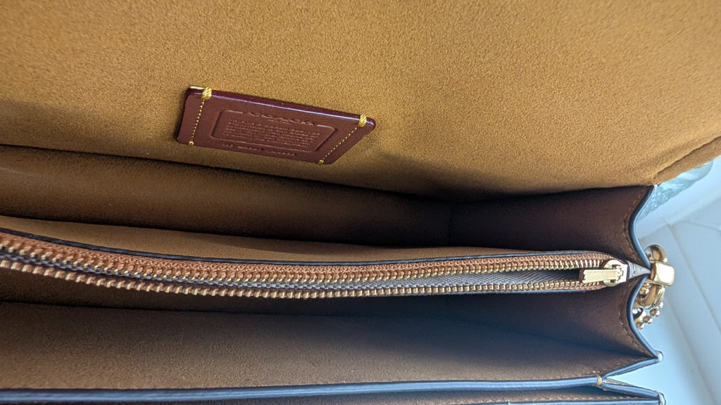 Close-up of the interior of a brown leather BAG showing a tan suede-like lining, a brown leather brand patch, and a silver-toned zipper. Pre-Owned Coach Tabby Braided Leather Shoulder Bag – Beige