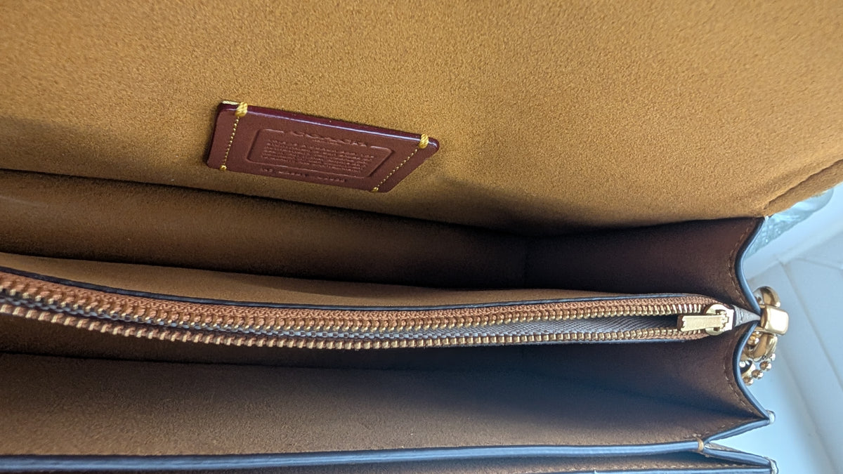 Close-up of the interior of a brown leather BAG showing a tan suede-like lining, a brown leather brand patch, and a silver-toned zipper. Pre-Owned Coach Tabby Braided Leather Shoulder Bag – Beige