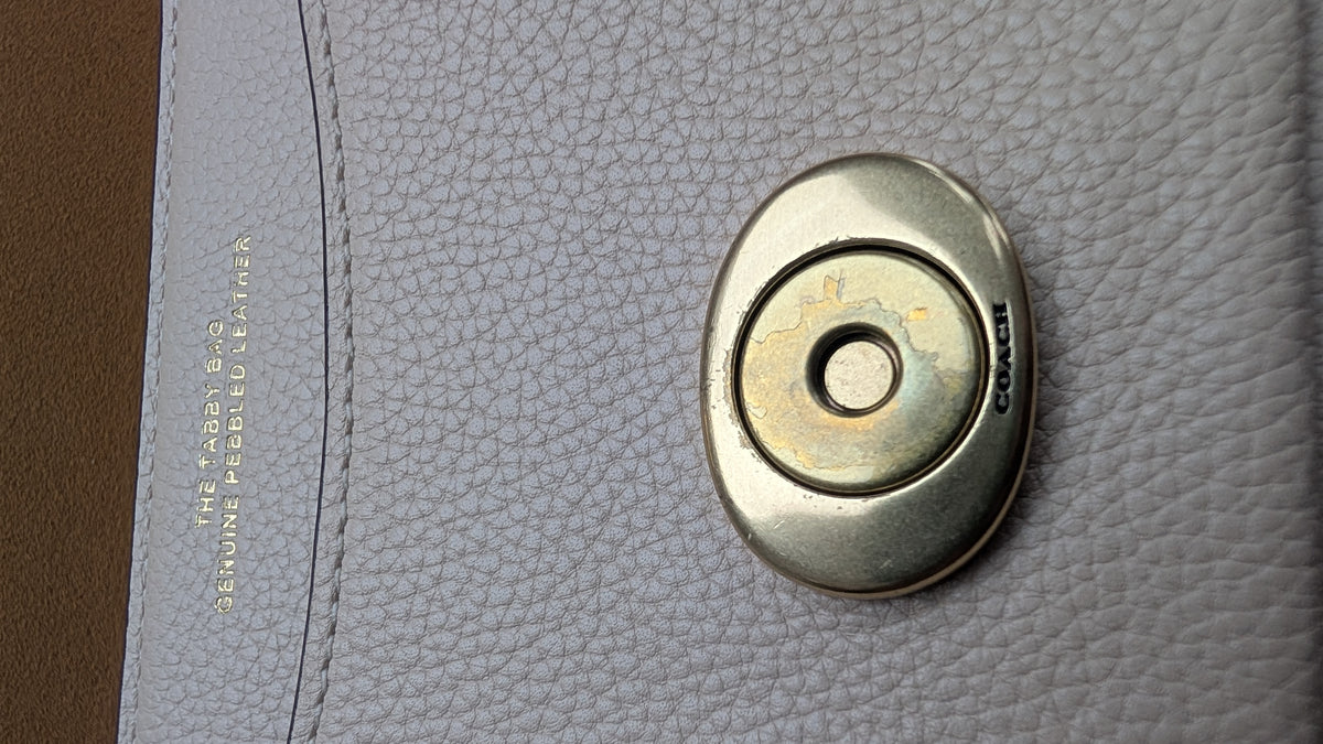 Close-up of a Coach leather bag showing a textured light gray pebbled leather surface,  Pre-Owned Coach Tabby Braided Leather Shoulder Bag – Beige