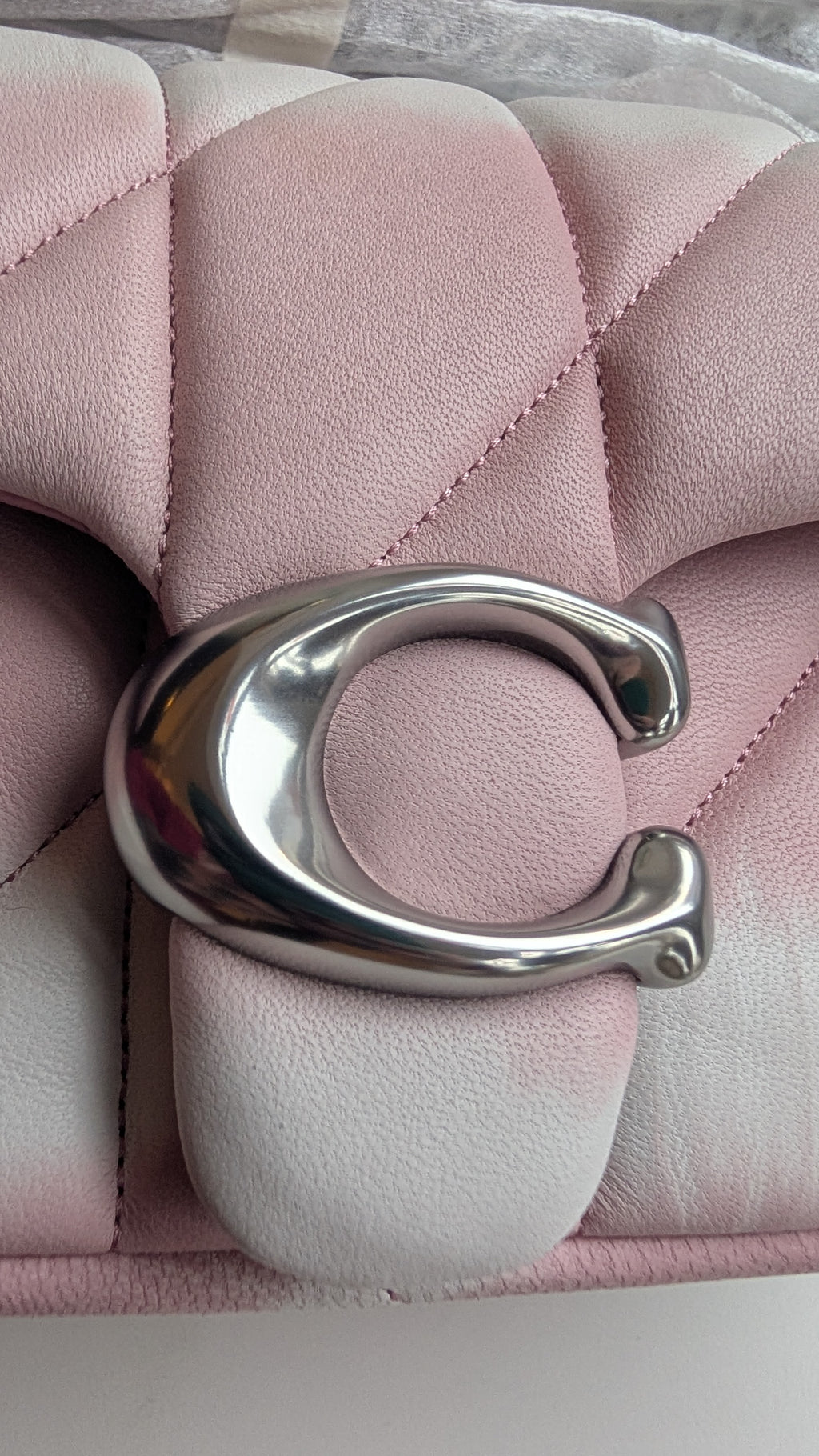 A close-up of a pink quilted leather handbag featuring a large polished silver-tone 'C' logo clasp, Pre-Owned Coach Tabby 20 Quilted Nappa Leather Shoulder Bag – Pink & White Ombré