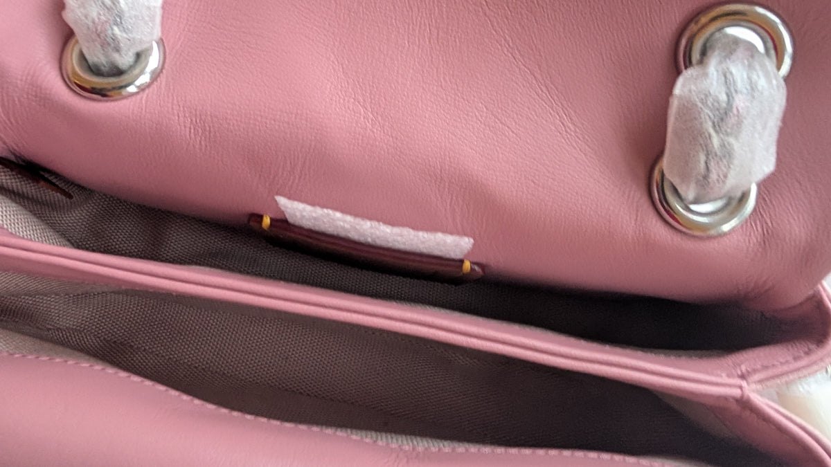 Close-up of a pink leather handbag showing the interior lining, silver-tone hardware with white protective paper still wrapped around the handles. Pre-Owned Coach Tabby 20 Quilted Nappa Leather Shoulder Bag – Pink & White Ombré