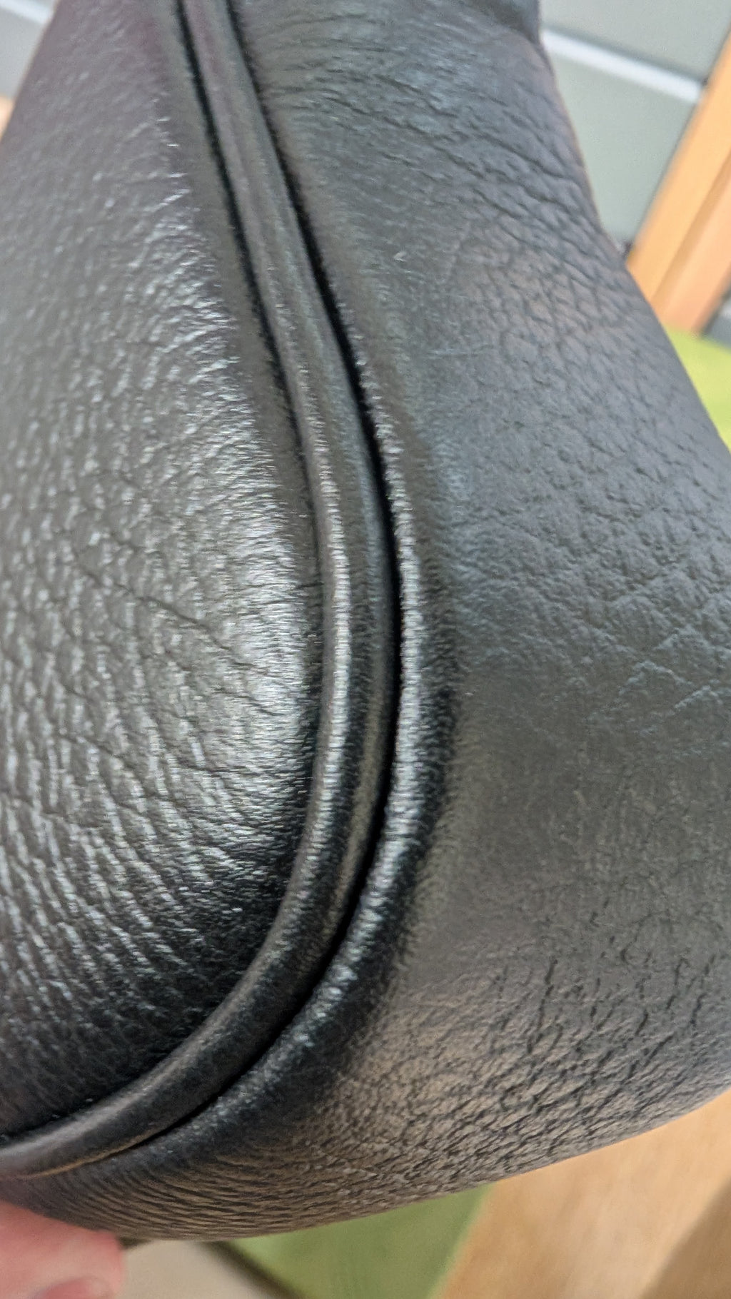 Close-up of a black pebbled leather bag corner with a curved seam and a small portion of a finger holding it at the bottom left. Pre-Owned Gucci GG Marmont Black Leather Camera Crossbody Bag – Gold Hardware