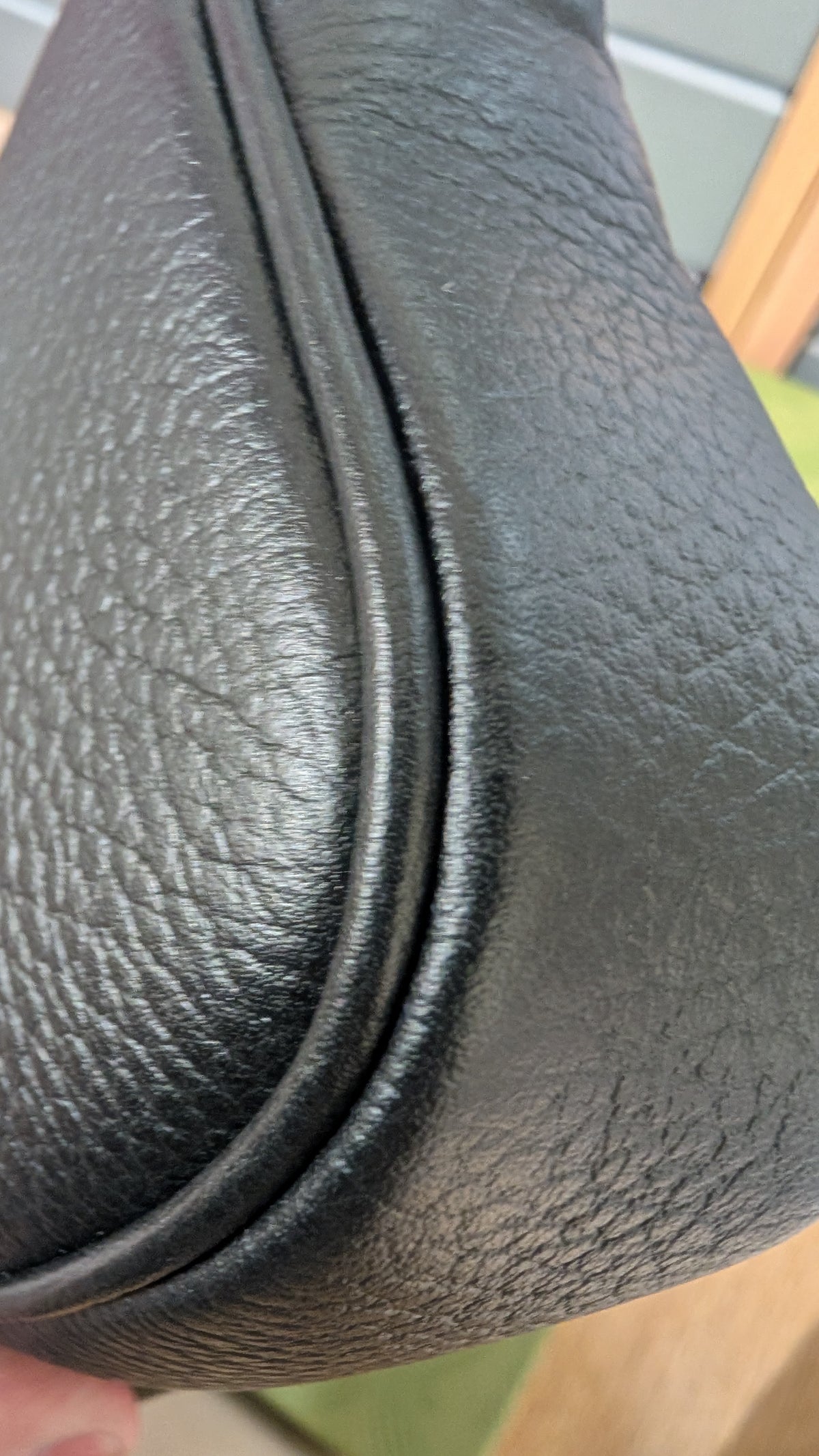 Close-up of a black pebbled leather bag corner with a curved seam and a small portion of a finger holding it at the bottom left. Pre-Owned Gucci GG Marmont Black Leather Camera Crossbody Bag – Gold Hardware