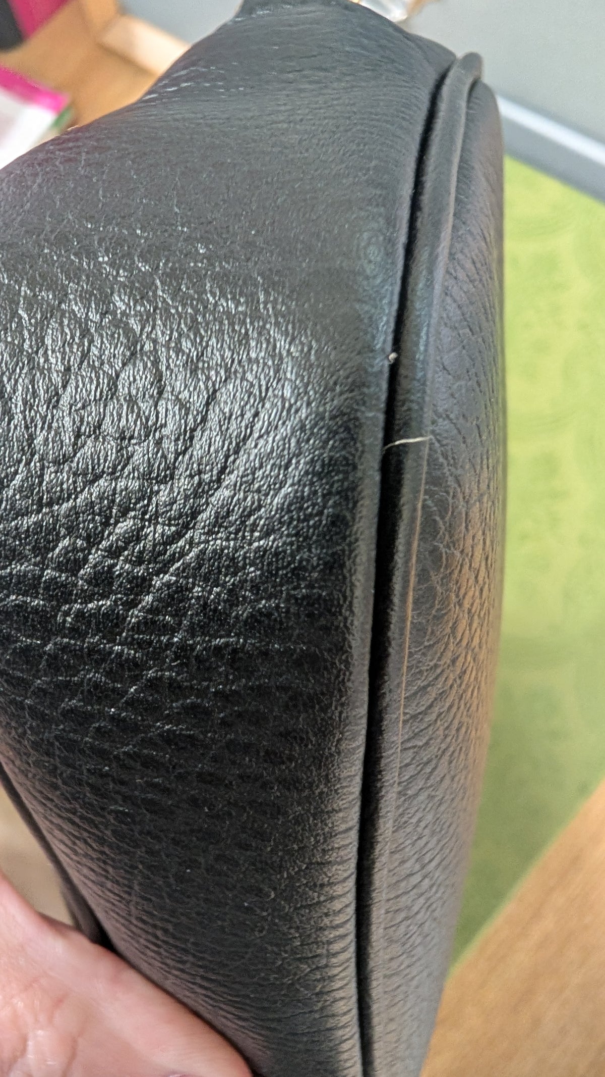 Close-up of a black textured leather bag corner held by a hand, showing the pebbled leather grain and a seam detail. Pre-Owned Gucci GG Marmont Black Leather Camera Crossbody Bag – Gold Hardware