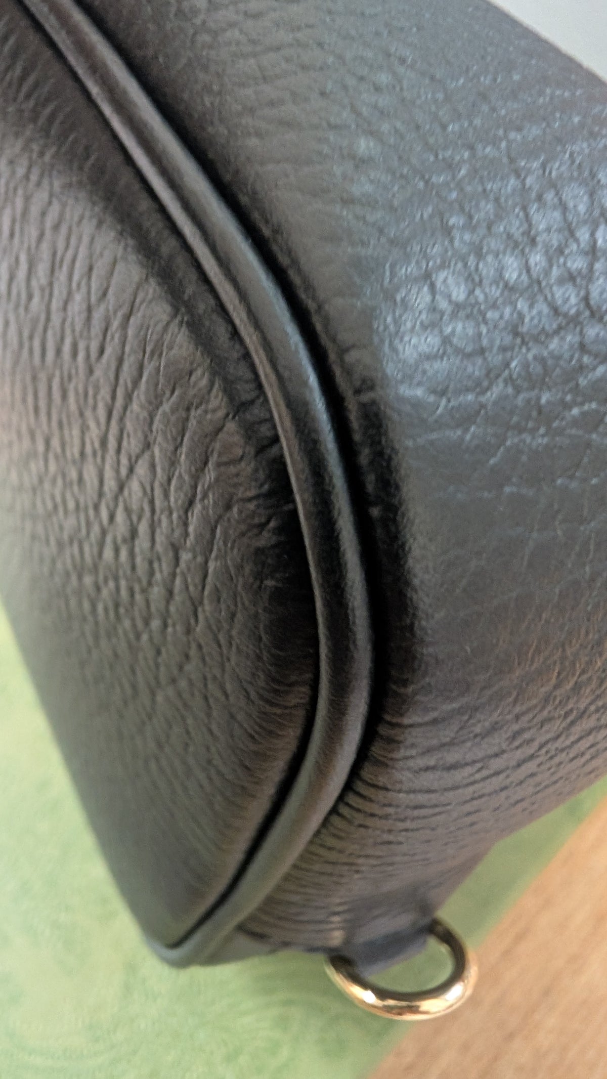 Close-up of a black pebbled leather bag corner showing a curved seam, textured surface, and a small gold-tone ring hardware detail. Pre-Owned Gucci GG Marmont Black Leather Camera Crossbody Bag – Gold Hardware