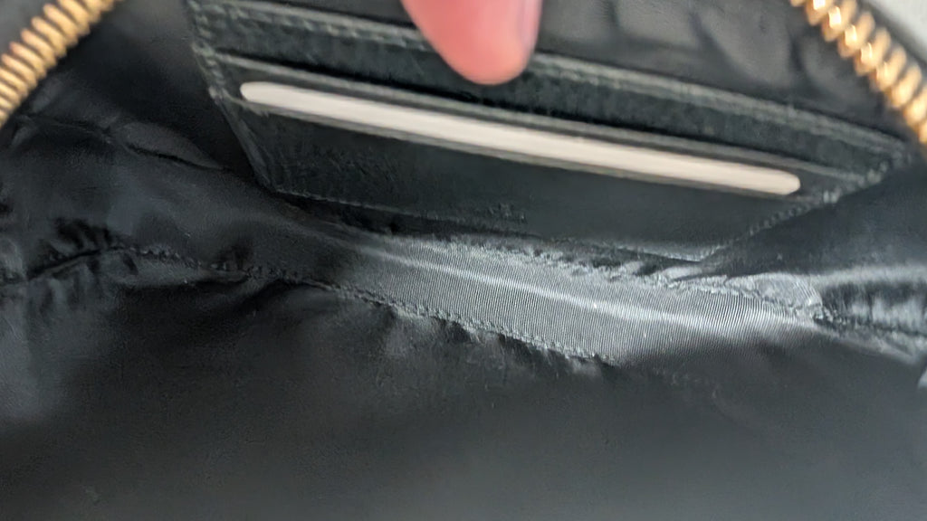 Close-up of the interior of a black nylon bag, showing a zippered pocket with gold-tone zipper trim and a finger pointing toward a card slot. Pre-Owned Gucci GG Marmont Black Leather Camera Crossbody Bag – Gold Hardware