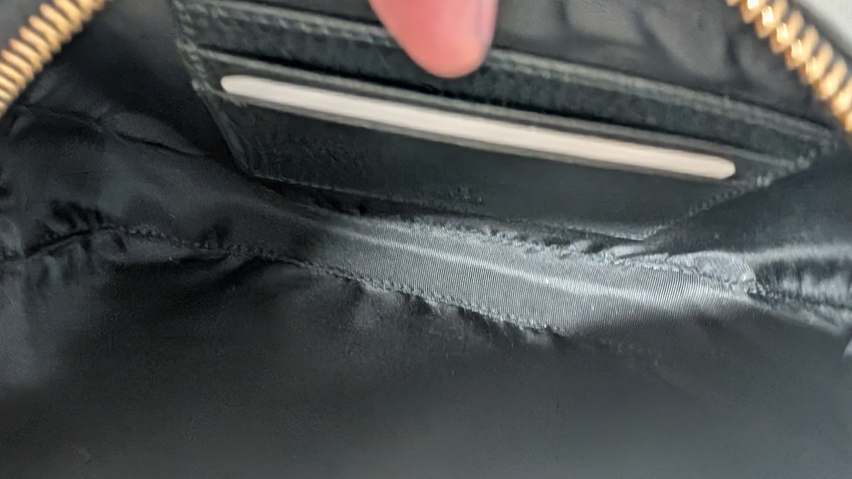Close-up of the interior of a black nylon bag, showing a zippered pocket with gold-tone zipper trim and a finger pointing toward a card slot. Pre-Owned Gucci GG Marmont Black Leather Camera Crossbody Bag – Gold Hardware