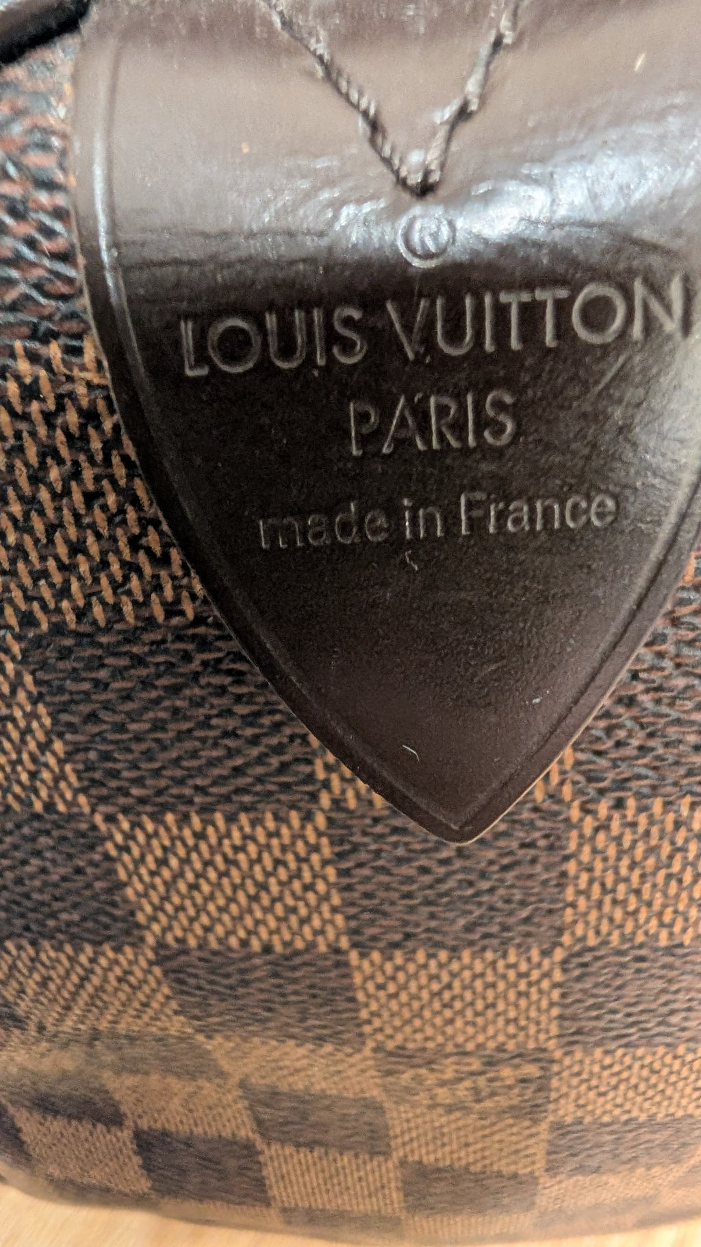 Close-up of a Louis Vuitton Paris made in France tag attached to a brown and beige checkered canvas bag. Pre-Owned Louis Vuitton Speedy 25 Damier Ebene Coated Canvas Bag DU4151