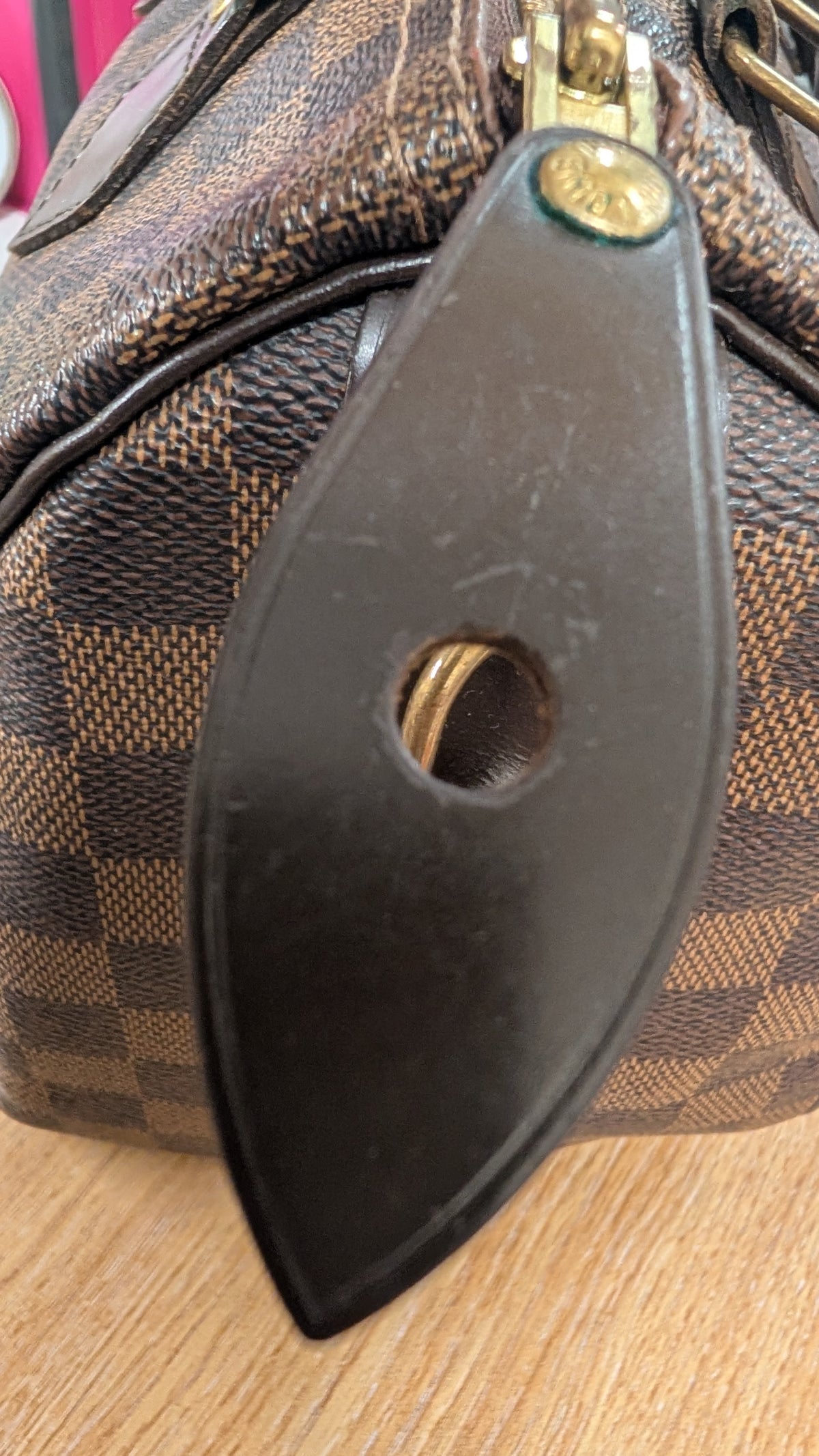 Close-up of a Louis Vuitton handbag in Damier Ebene canvas with a black leather strap and gold-tone hardware, resting on a light wood surface. Pre-Owned Louis Vuitton Speedy 25 Damier Ebene Coated Canvas Bag DU4151