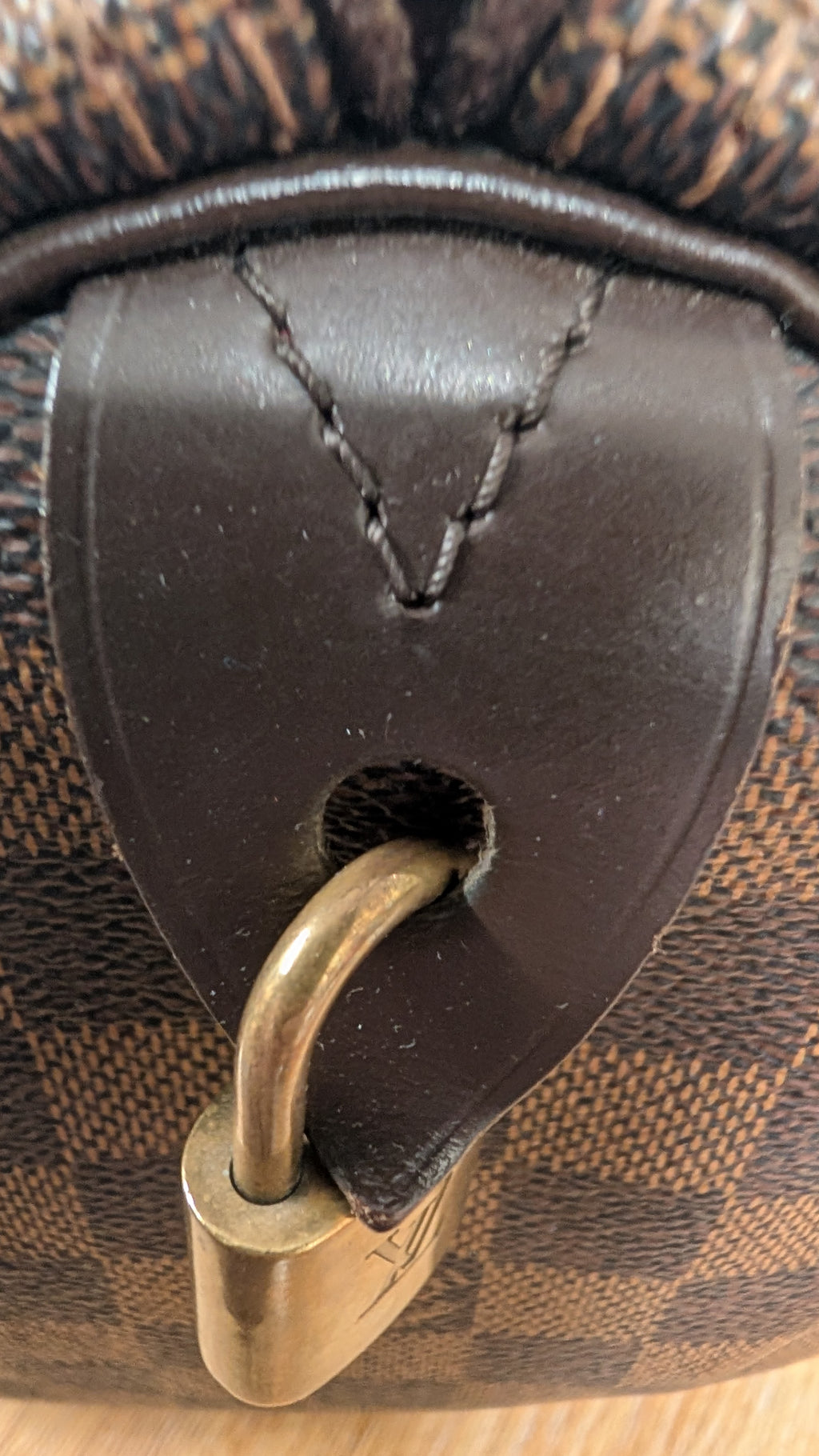 Close-up of a Louis Vuitton handbag featuring the brand's classic Damier Ebene canvas and dark brown leather trim, secured with a brass padlock. Pre-Owned Louis Vuitton Speedy 25 Damier Ebene Coated Canvas Bag DU4151